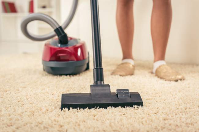 A woman is using a vacuum cleaner to clean a carpet.