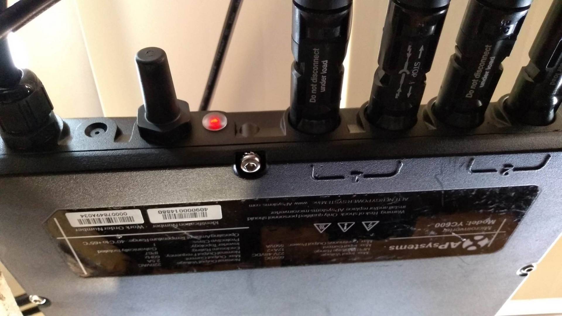 Imagem em close-up de um Micro inversor com portas, etiquetas e luzes indicadoras sobre uma mesa.