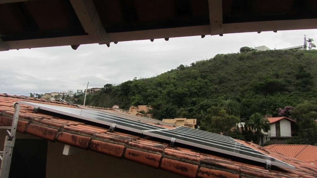 Telhados em primeiro plano com uma encosta verde e céu nublado ao fundo.