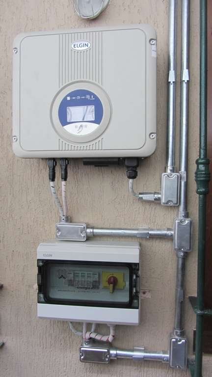 Inversor montado na parede, com tubulações e fios expostos em uma parede bege.