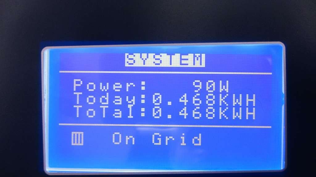 Tela LCD azul exibindo o status de energia do sistema, as leituras de kWh atuais e totais, com a mensagem “On Grid” (Conectado à Rede).