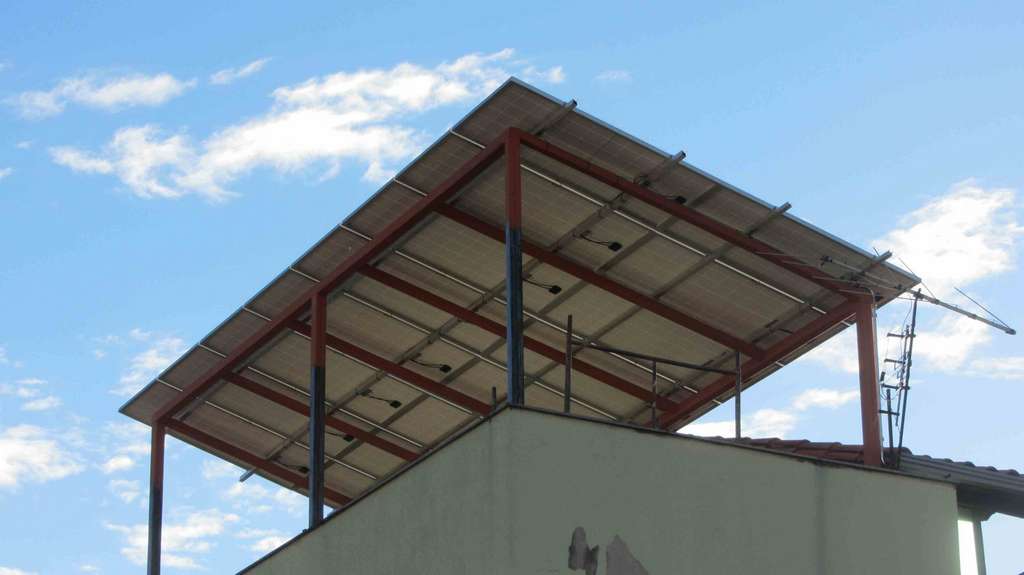 Telhado com uma grande cobertura metálica contra um céu azul com nuvens.