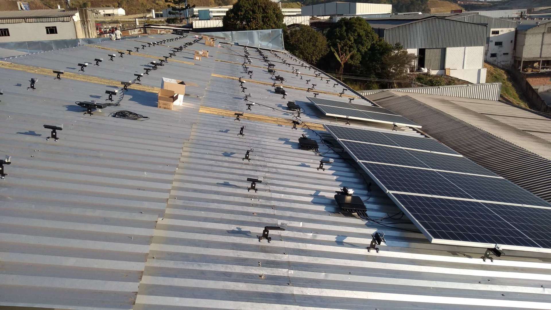 Telhado com painéis solares e aberturas de ventilação em uma cobertura metálica ondulada sob forte luz solar.