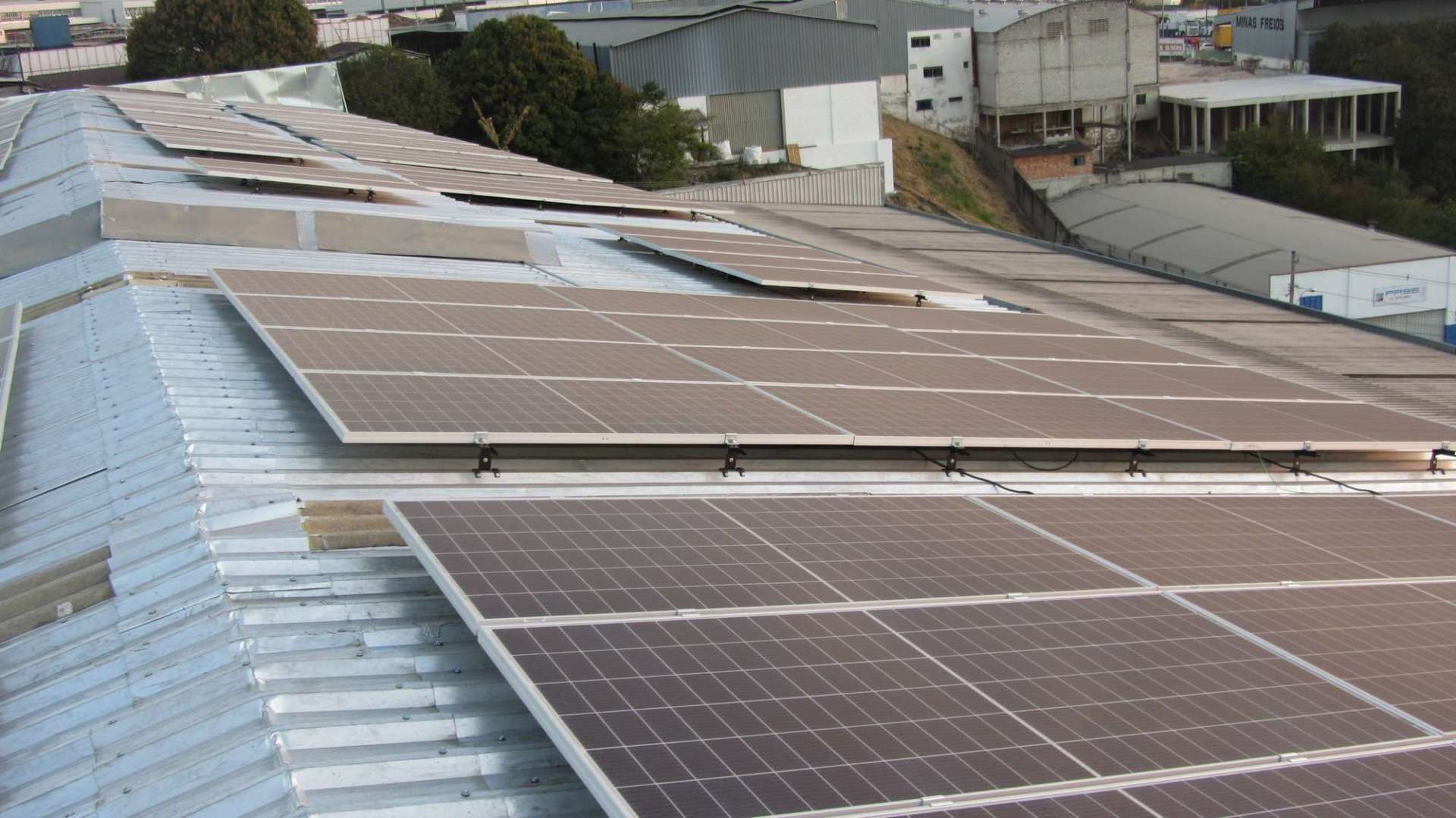 Painéis solares instalados em um telhado metálico em uma área industrial.