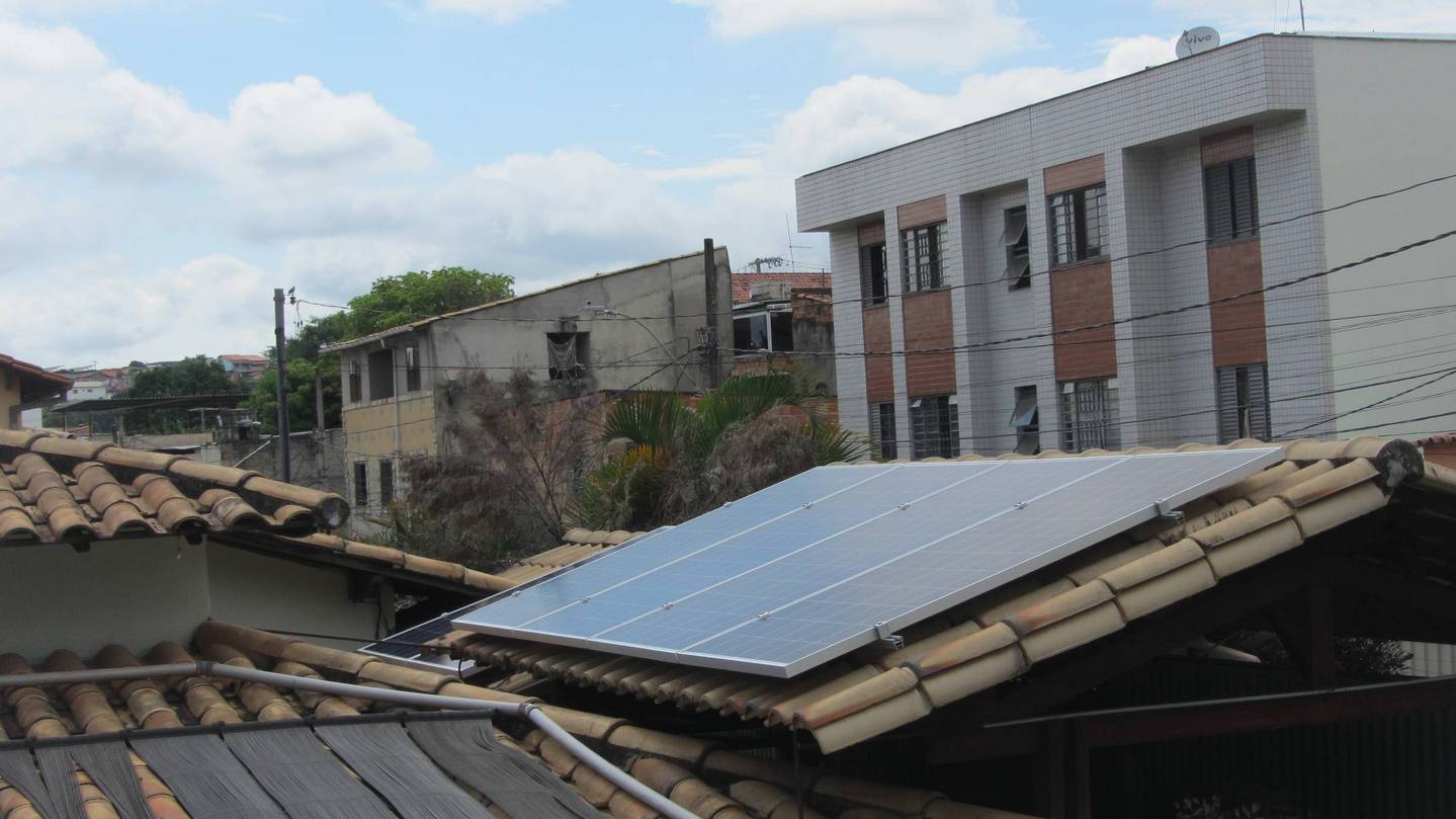 Painéis solares instalados no telhado de um prédio em um bairro residencial sob um céu nublado.