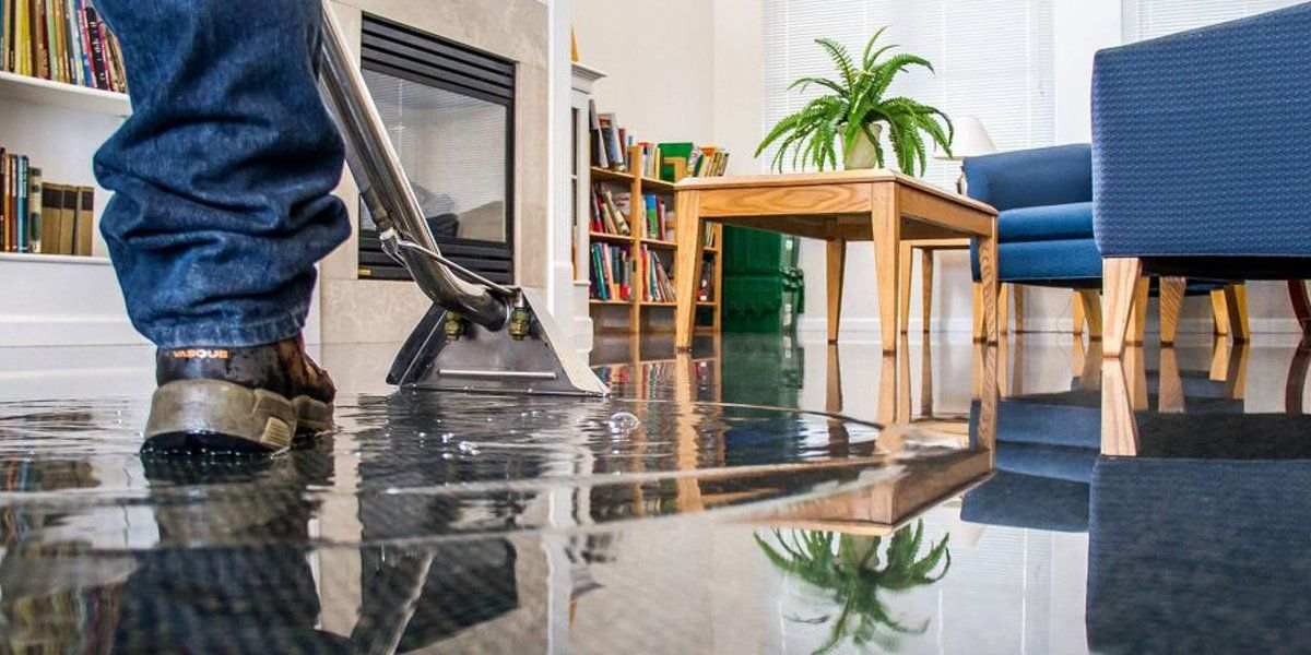 A man is using a vacuum cleaner to clean a flooded floor in a living room.