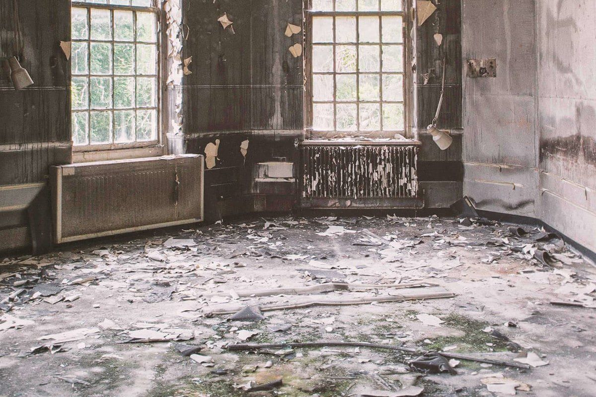 An empty room with a lot of trash on the floor and walls.