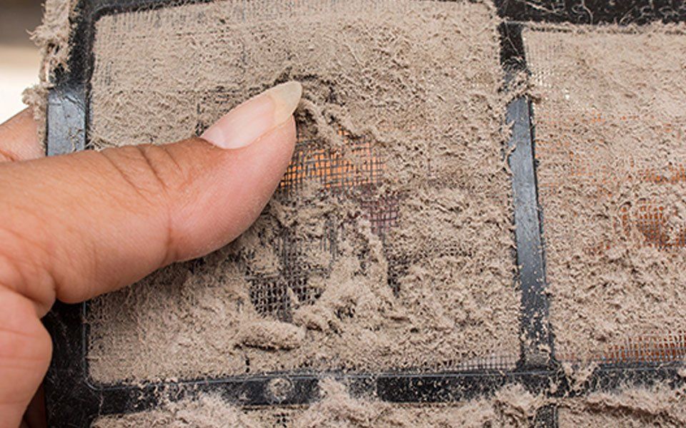 A person is cleaning a dirty air filter with their finger.