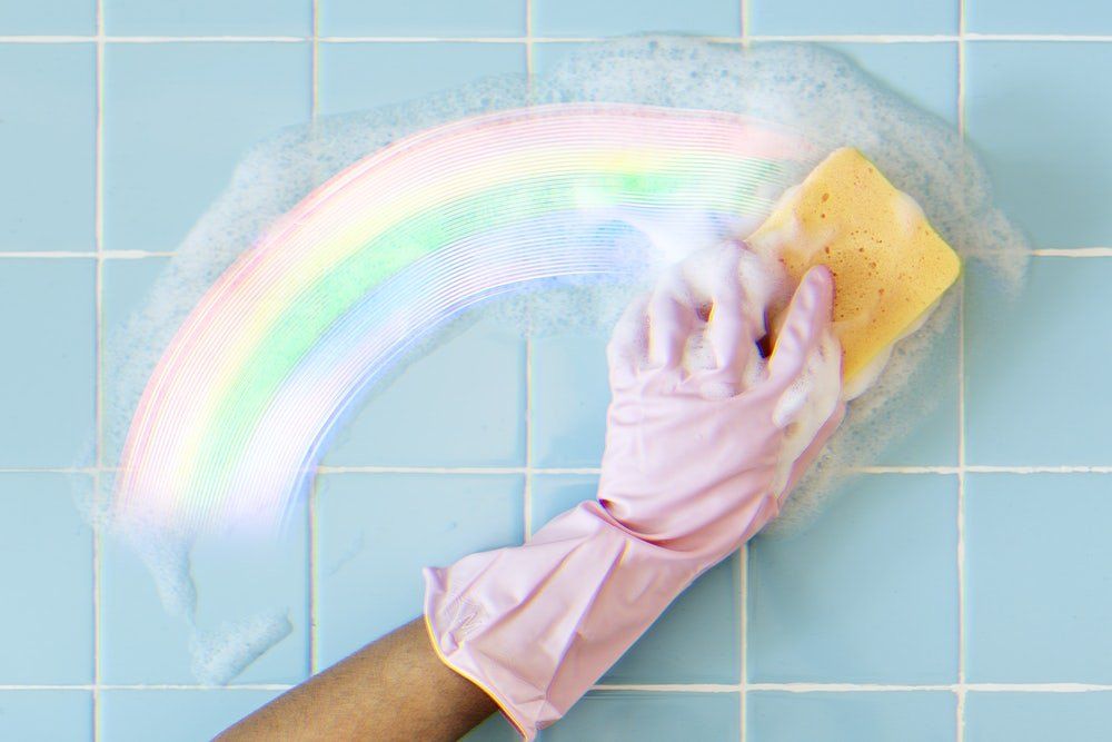 A person wearing pink gloves is cleaning a tile wall with a sponge.