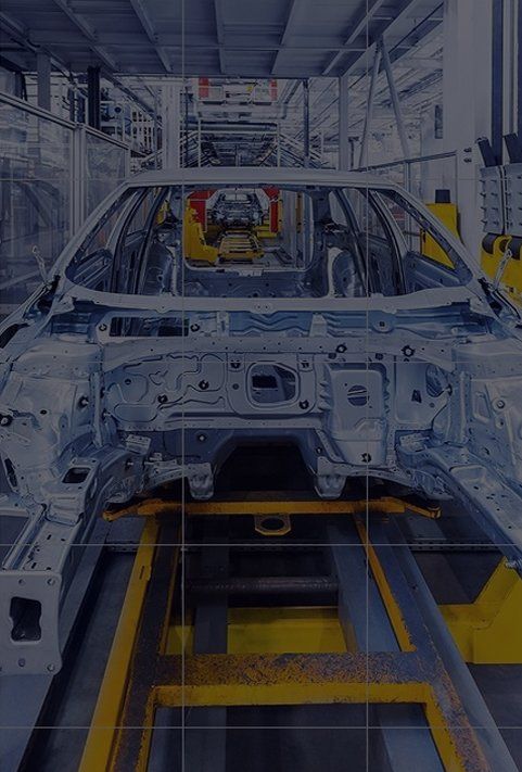 A car chassis moving along an industrial assembly line, featuring metal frame construction and yellow support rails.