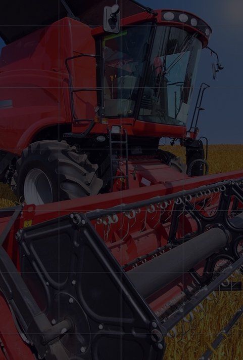 A red combine harvester works in a golden wheat field during the day.