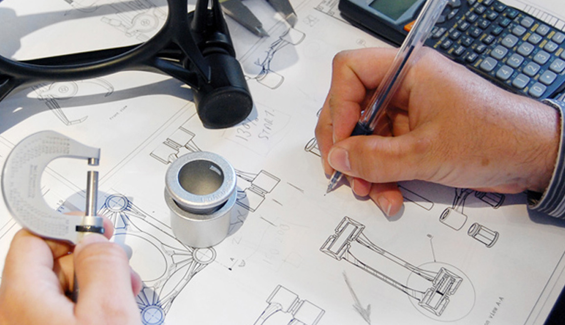 Hands holding a micrometer and a pen over technical engineering blueprints with a cylindrical part and a calculator.