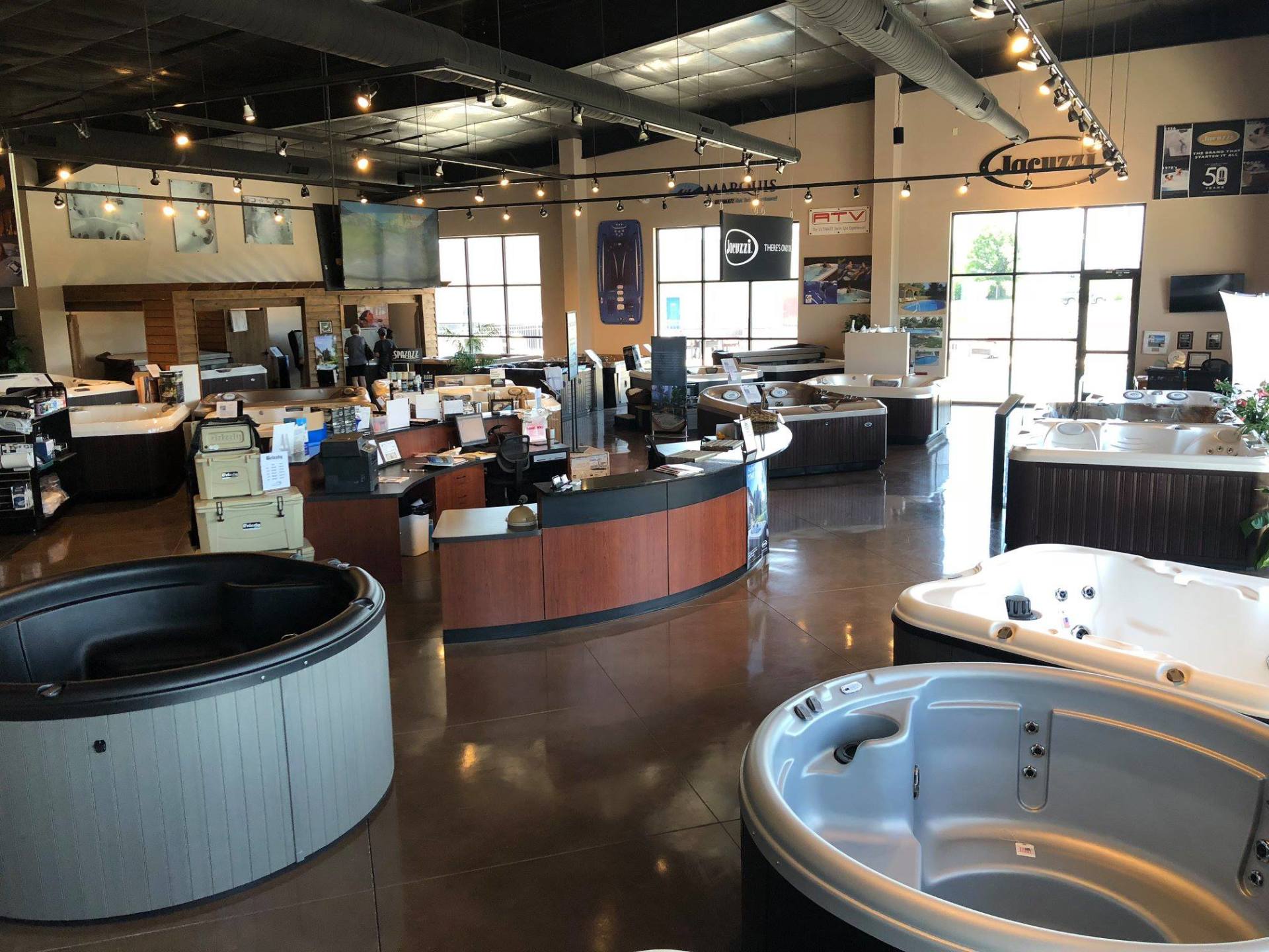 Showroom with hot tubs and spa displays under warm lighting, featuring a curved reception counter.