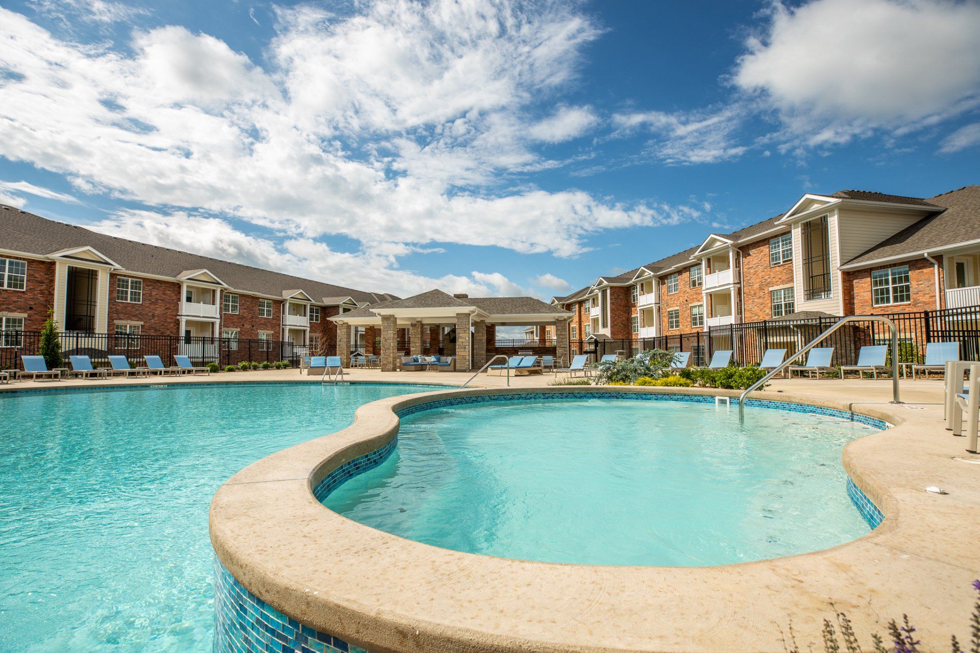 Apartment complex pool with curved turquoise water and brick townhomes under a blue sky