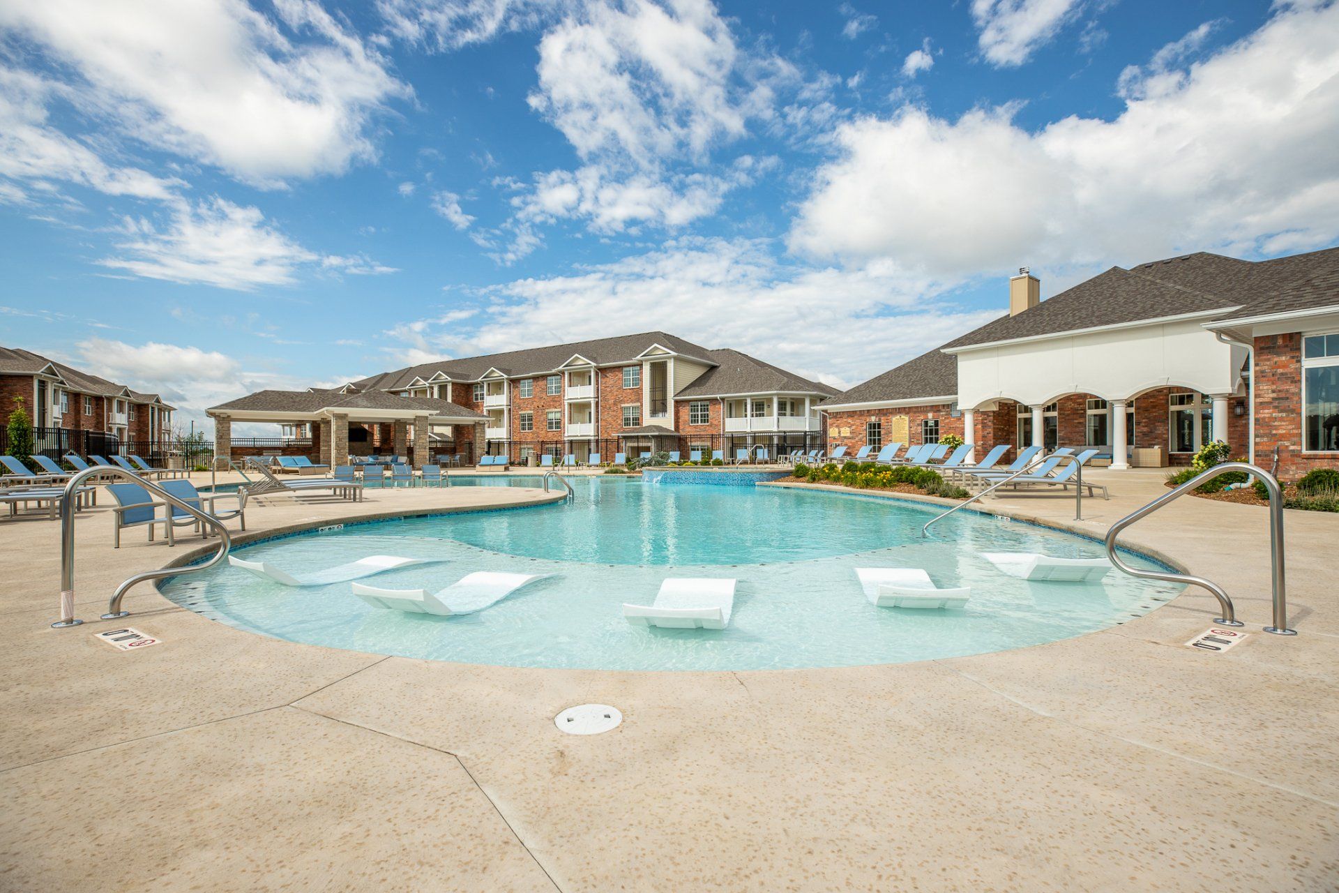 Apartment complex pool with a circular fountain under a partly cloudy sky