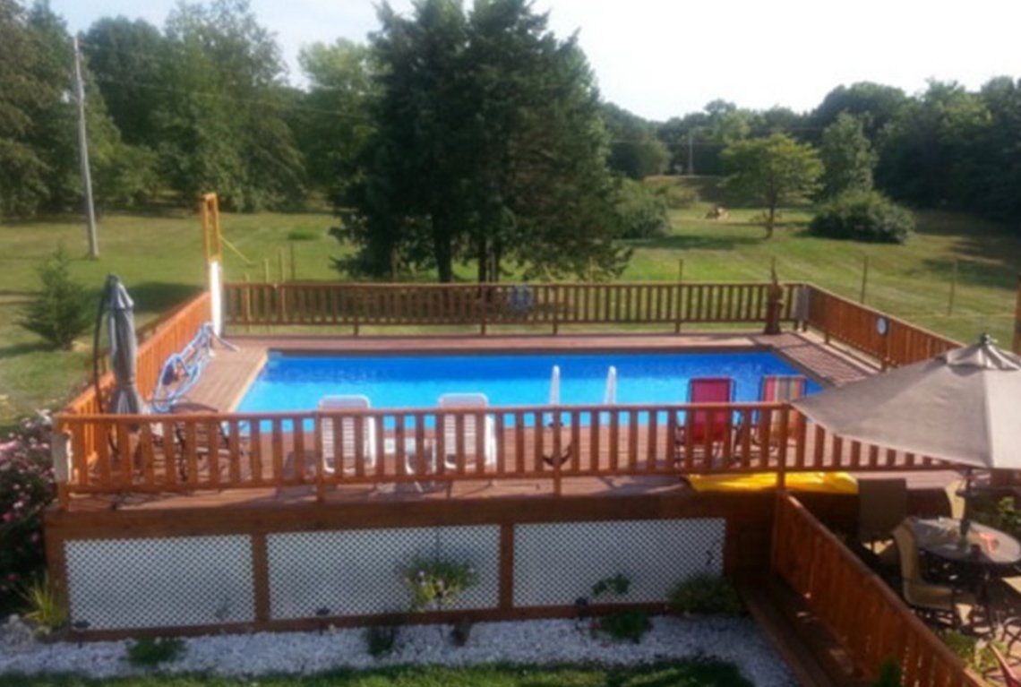 Backyard swimming pool with wooden deck, fence, and green lawn beyond