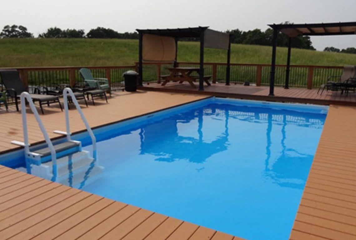 Outdoor swimming pool with wooden deck, metal ladder, and covered seating area in the background
