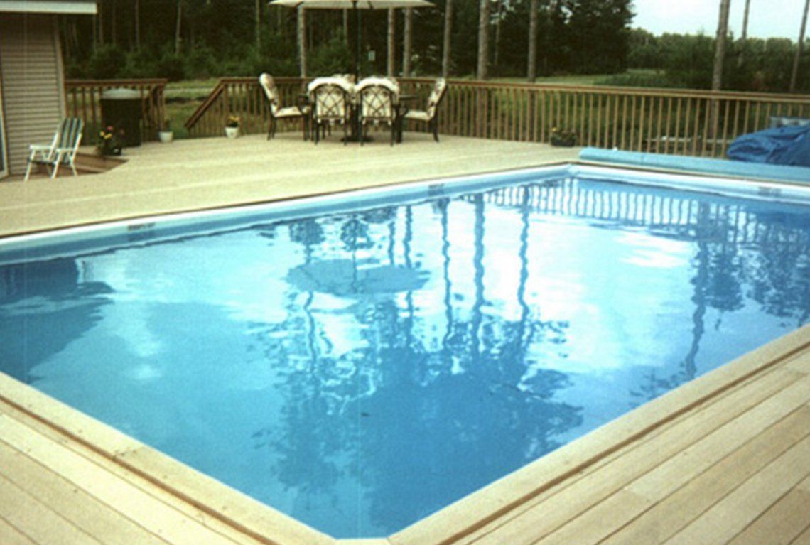 Backyard swimming pool with blue water and wooden deck by a fence and patio seating
