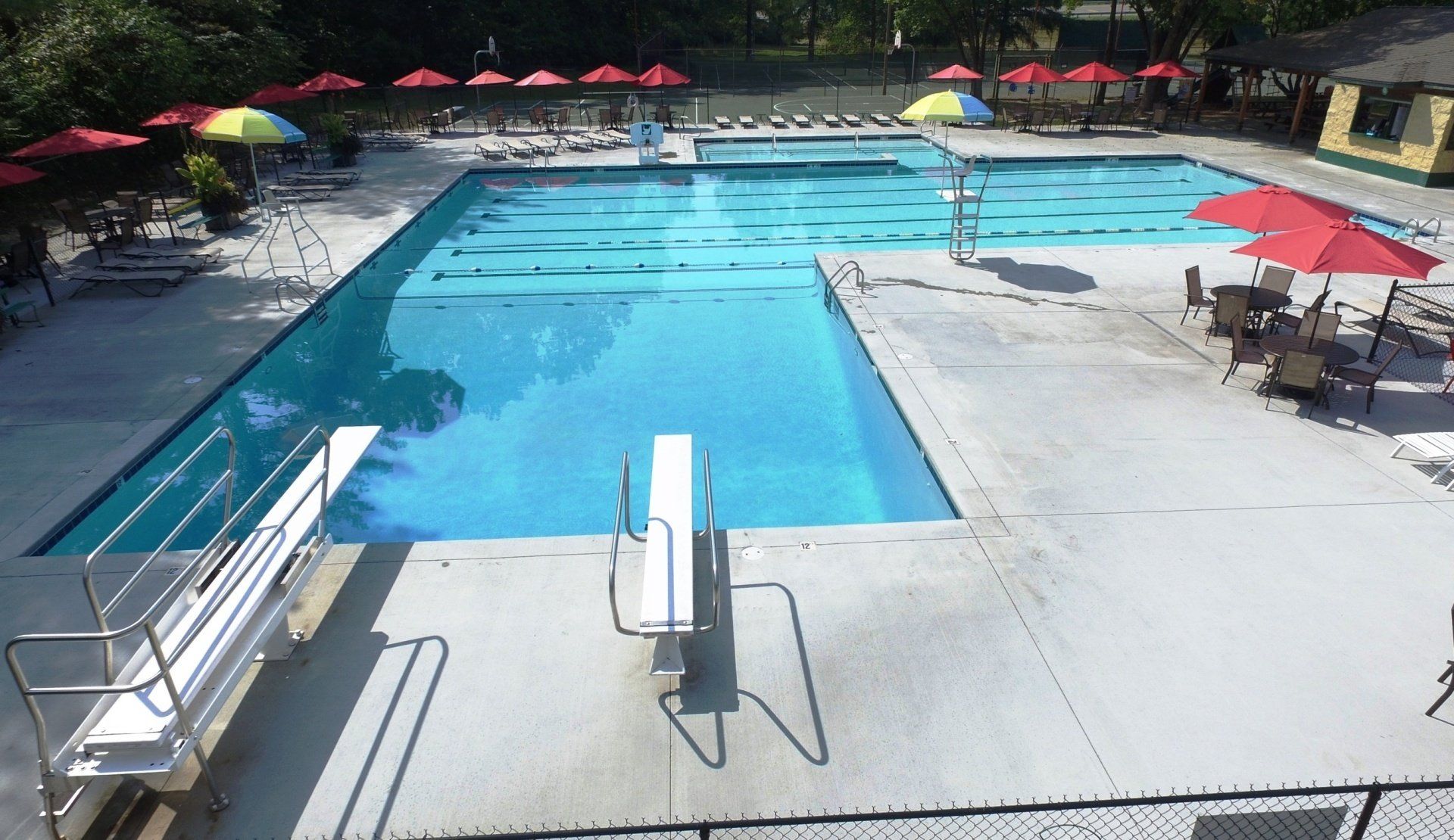 Outdoor swimming pool with blue water, white deck, red umbrellas, and lounge chairs.