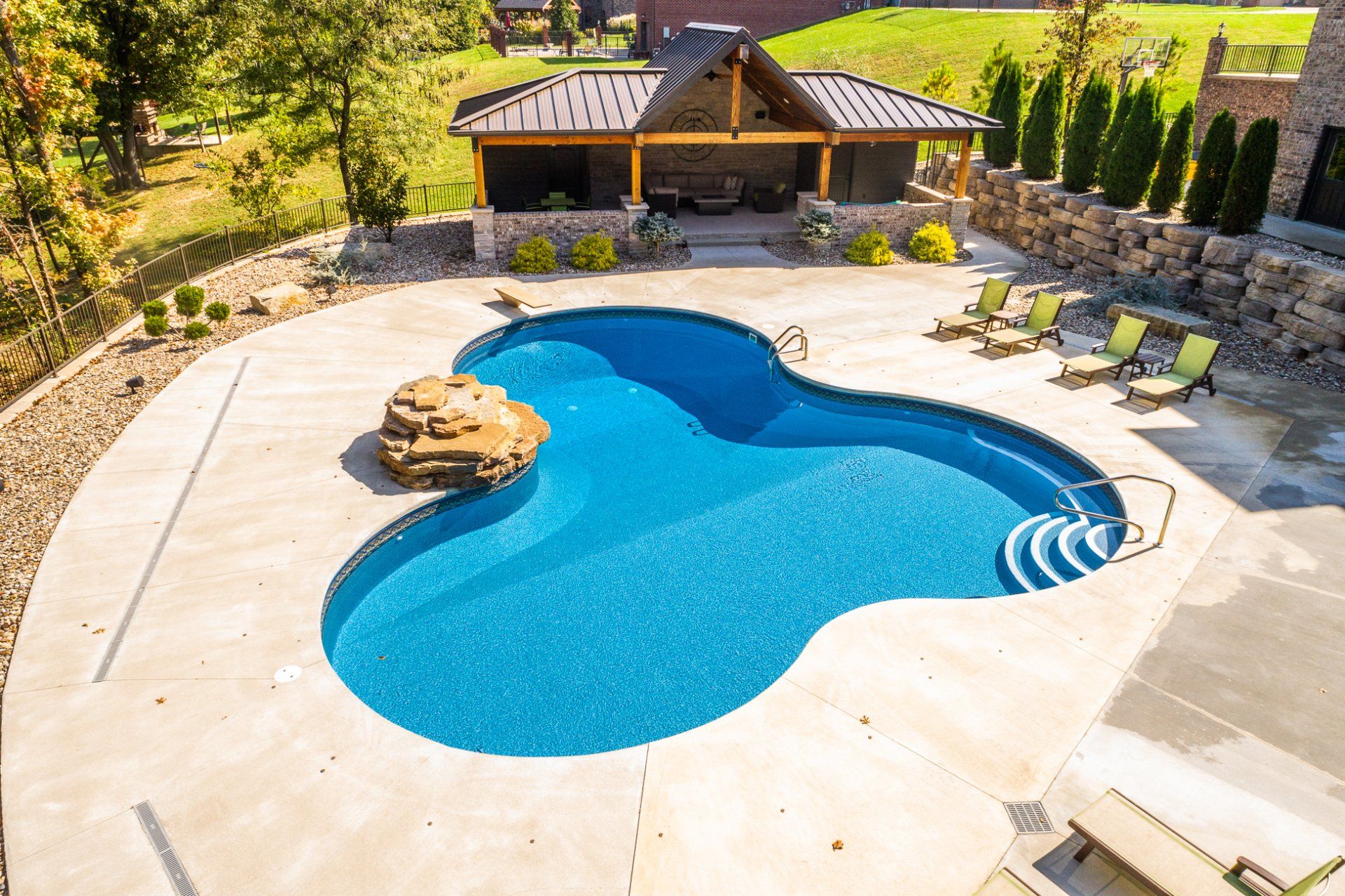 Backyard swimming pool with stone deck, lounge chairs, and a rustic cabana