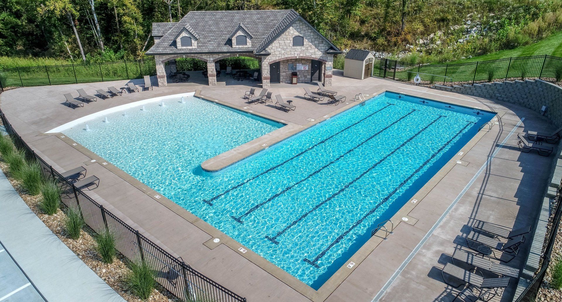 Outdoor swimming pool with diving board and adjacent covered patio, surrounded by lounge chairs and greenery