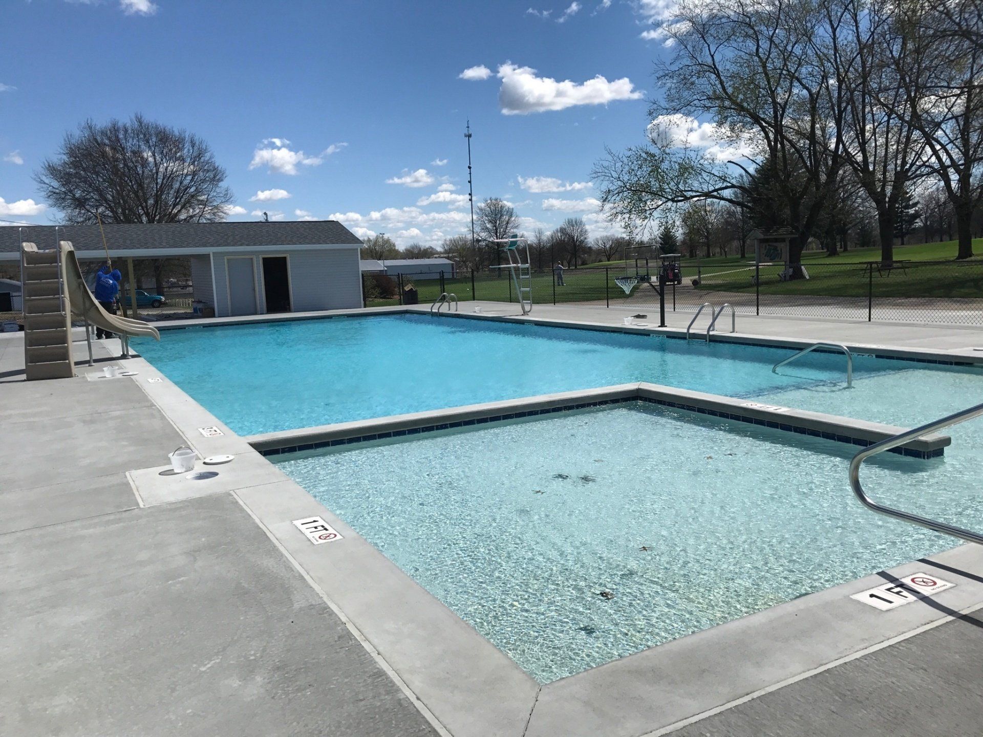 Outdoor swimming pool with a shallow wading area, concrete deck, and blue sky on a sunny day