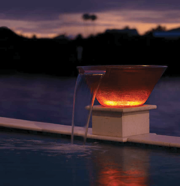 A bowl with a light inside of it sits next to a pool at night