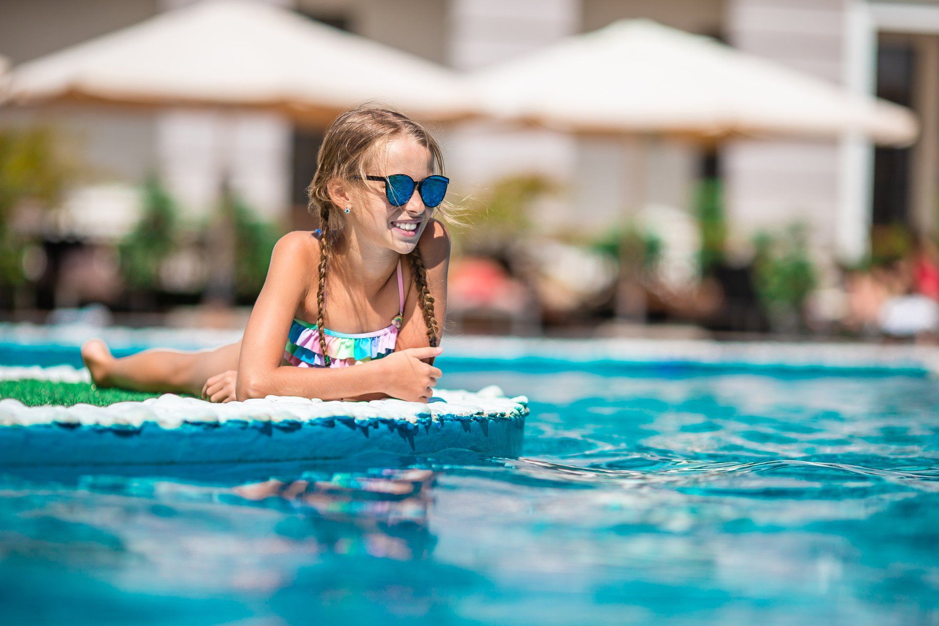 A little girl is laying on a raft in a swimming pool.