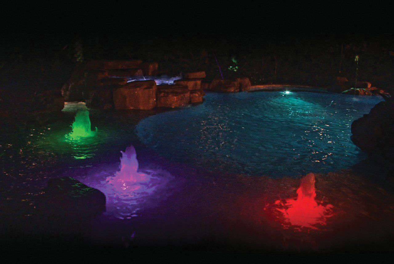 A swimming pool is lit up at night with colorful lights.