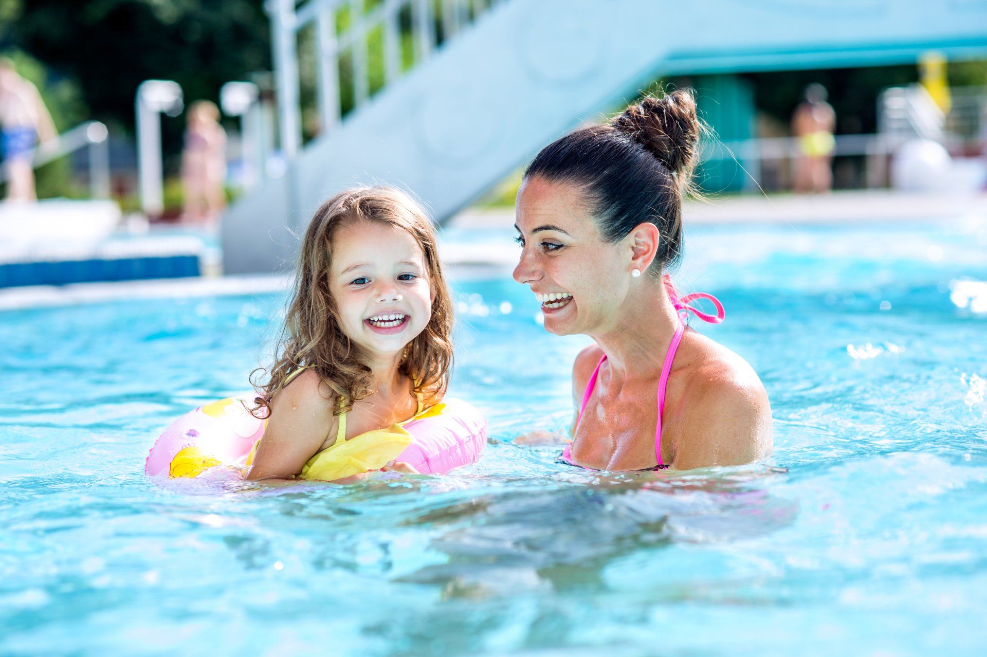 A woman and a little girl are playing in a swimming pool.