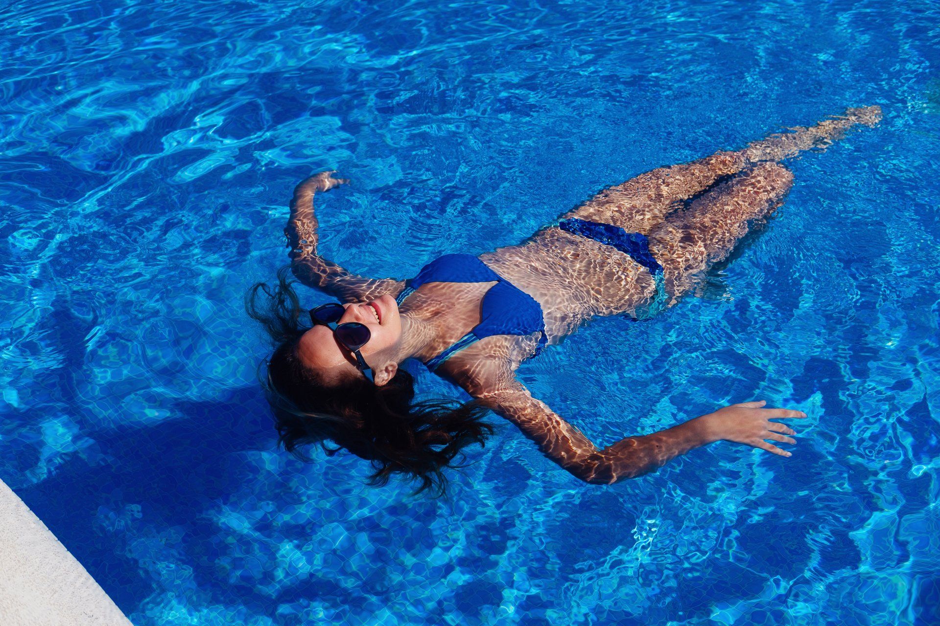 A woman in a blue bikini is floating on her back in a swimming pool.