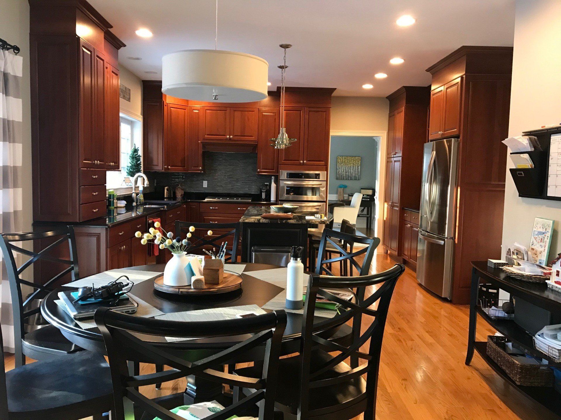 Modern kitchen with dark wood cabinets, black appliances, and a round dining table in the foreground