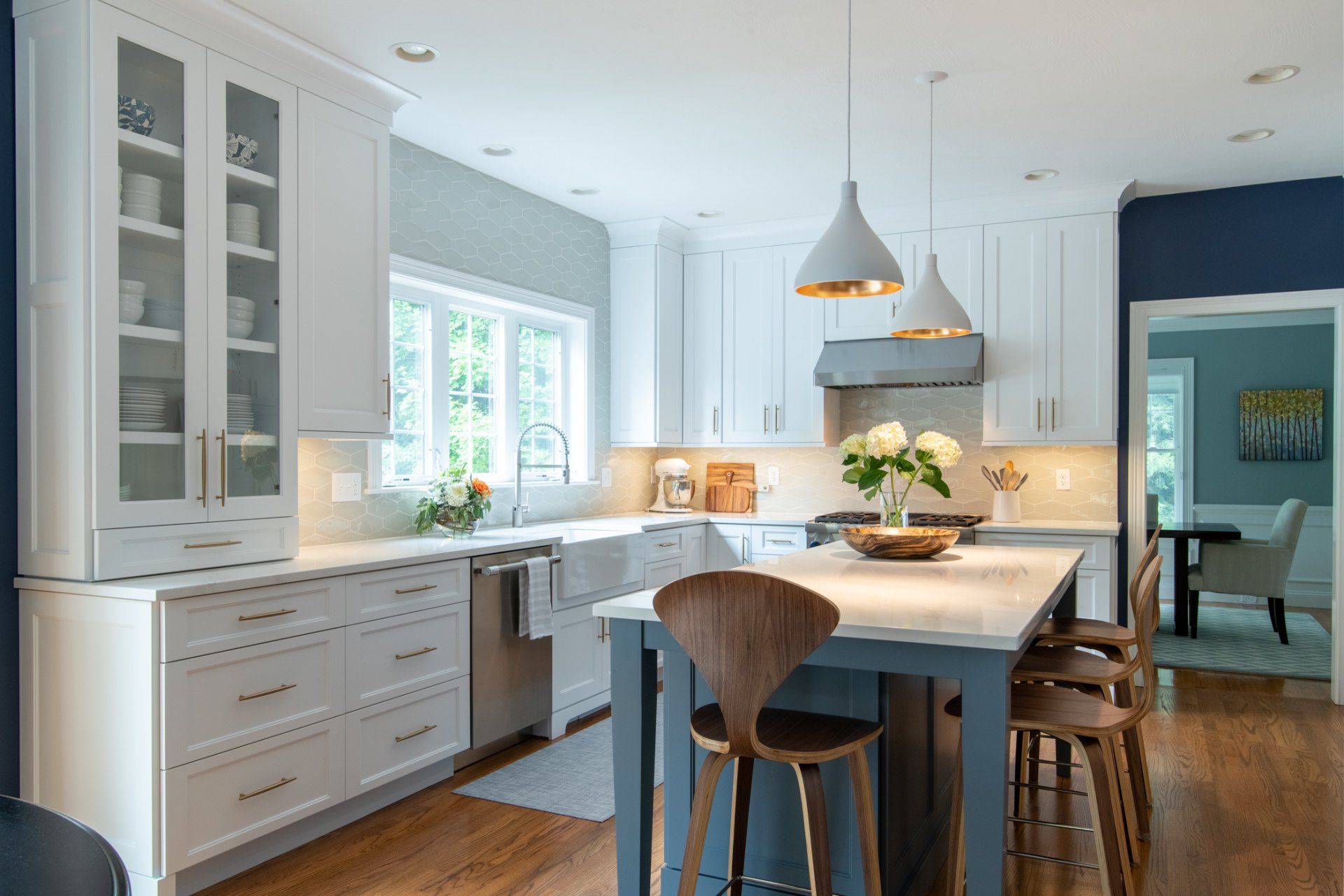 Bright white kitchen with island, blue accents, and large windows letting in natural light