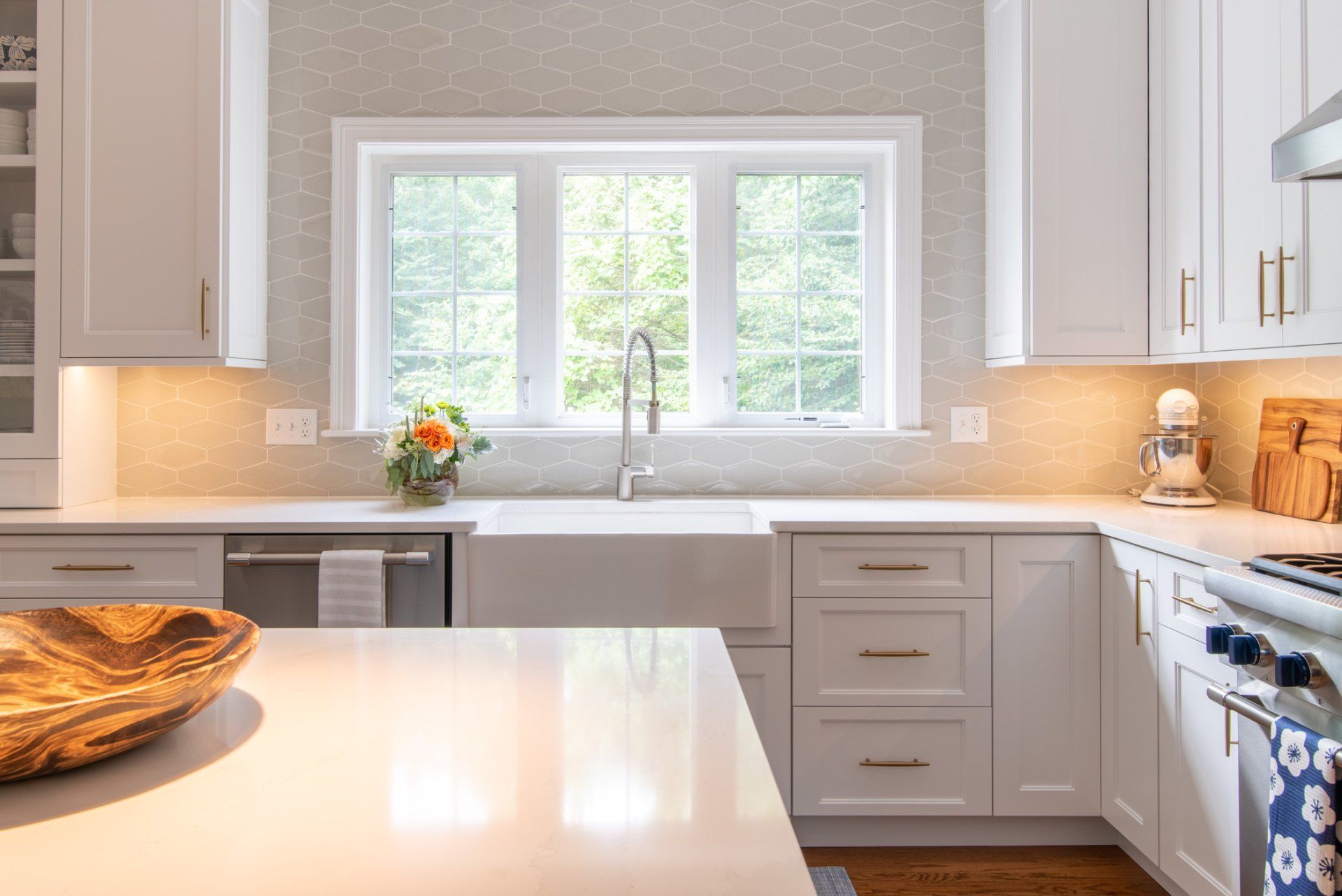 Bright kitchen with white cabinets, island, large window over sink, and blue stove with warm lighting