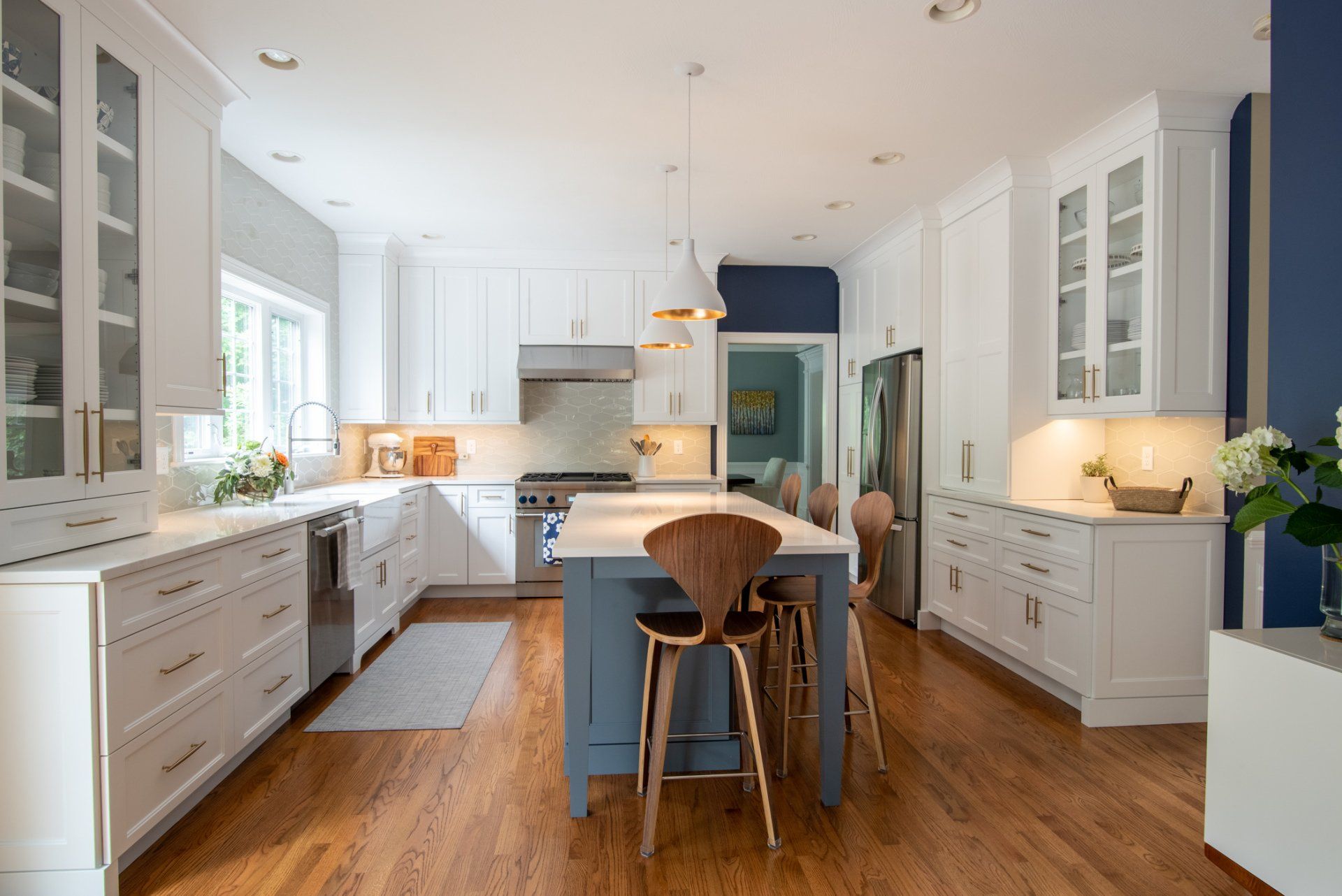 Bright white kitchen with blue island, wood floors, pendant lights, and glass-front cabinets