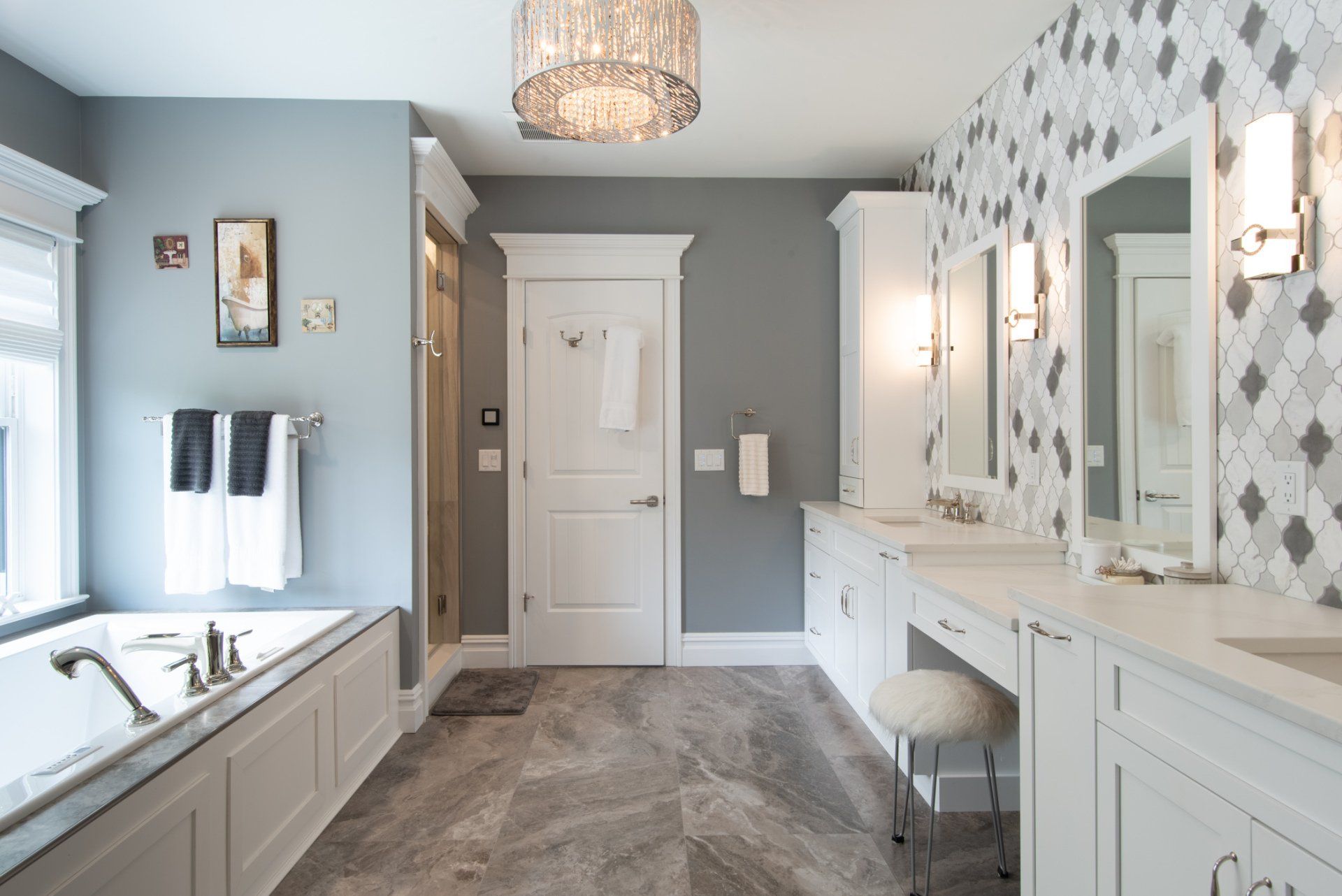 Spacious gray-and-white bathroom with double vanity, soaking tub, walk-in shower, and chandelier.