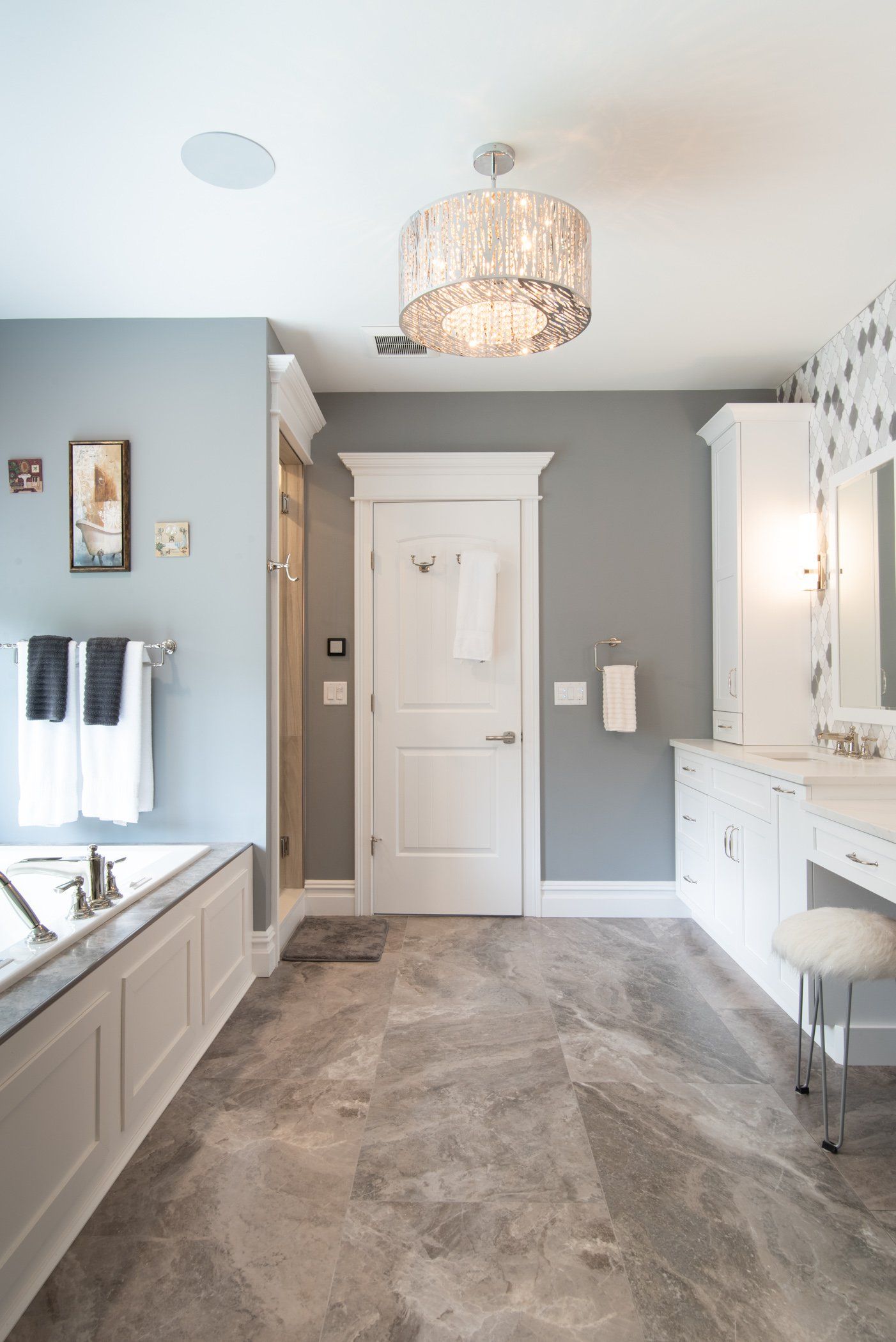 Bright bathroom with gray walls, white vanity and tub, a chandelier, and a closed white door.