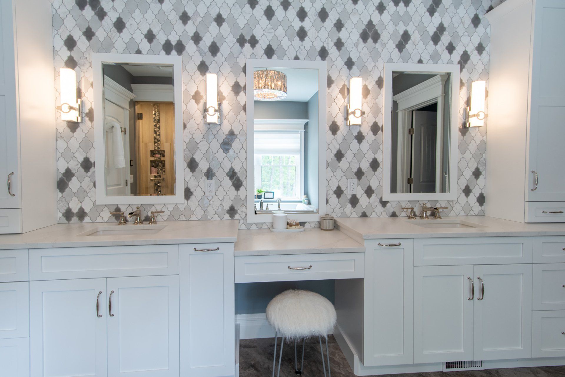 Elegant white bathroom vanity with three mirrors, patterned tile backsplash, and wall sconces