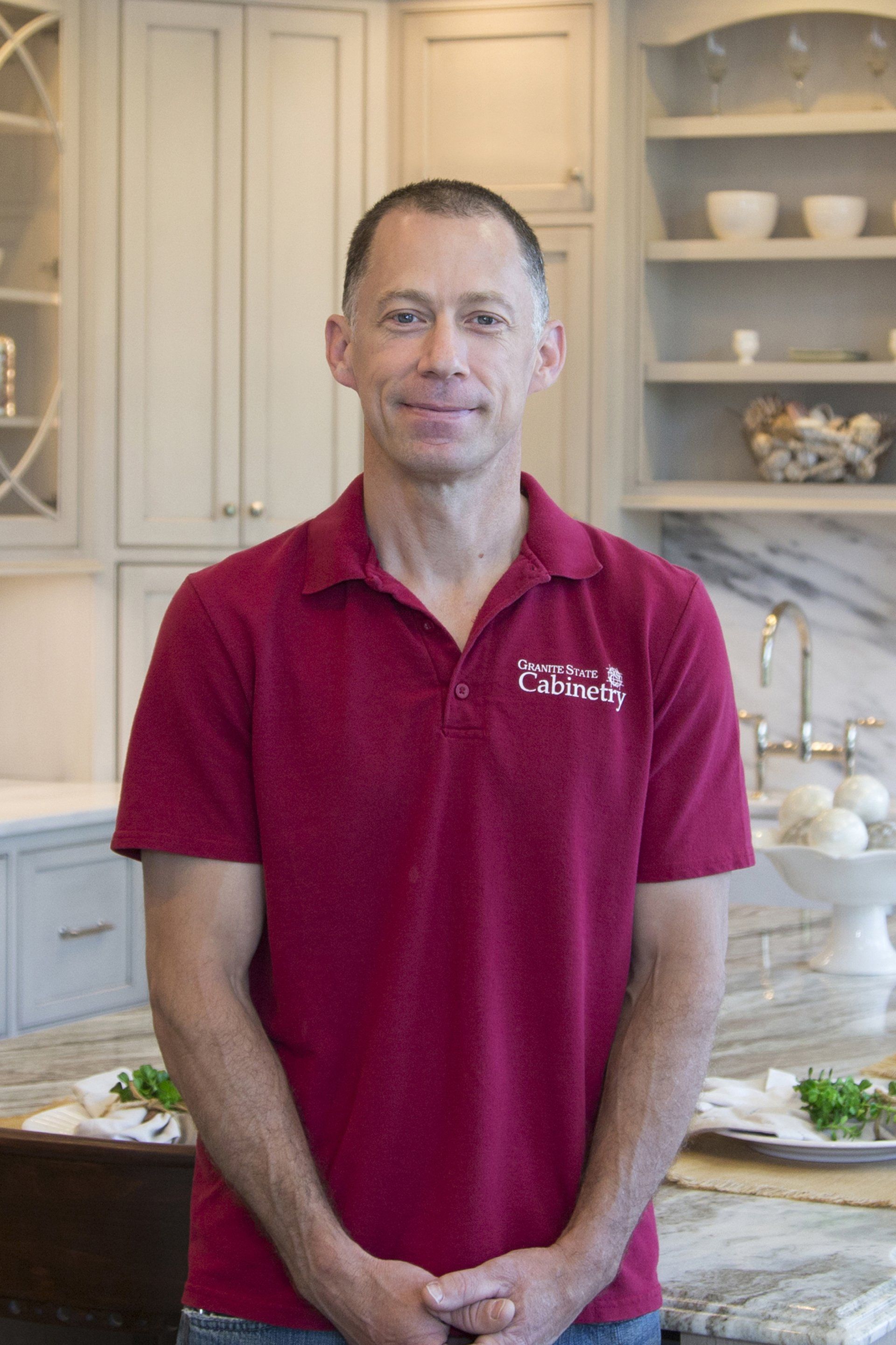 Man in a red polo shirt standing in a bright kitchen beside a countertop with plates and bowls