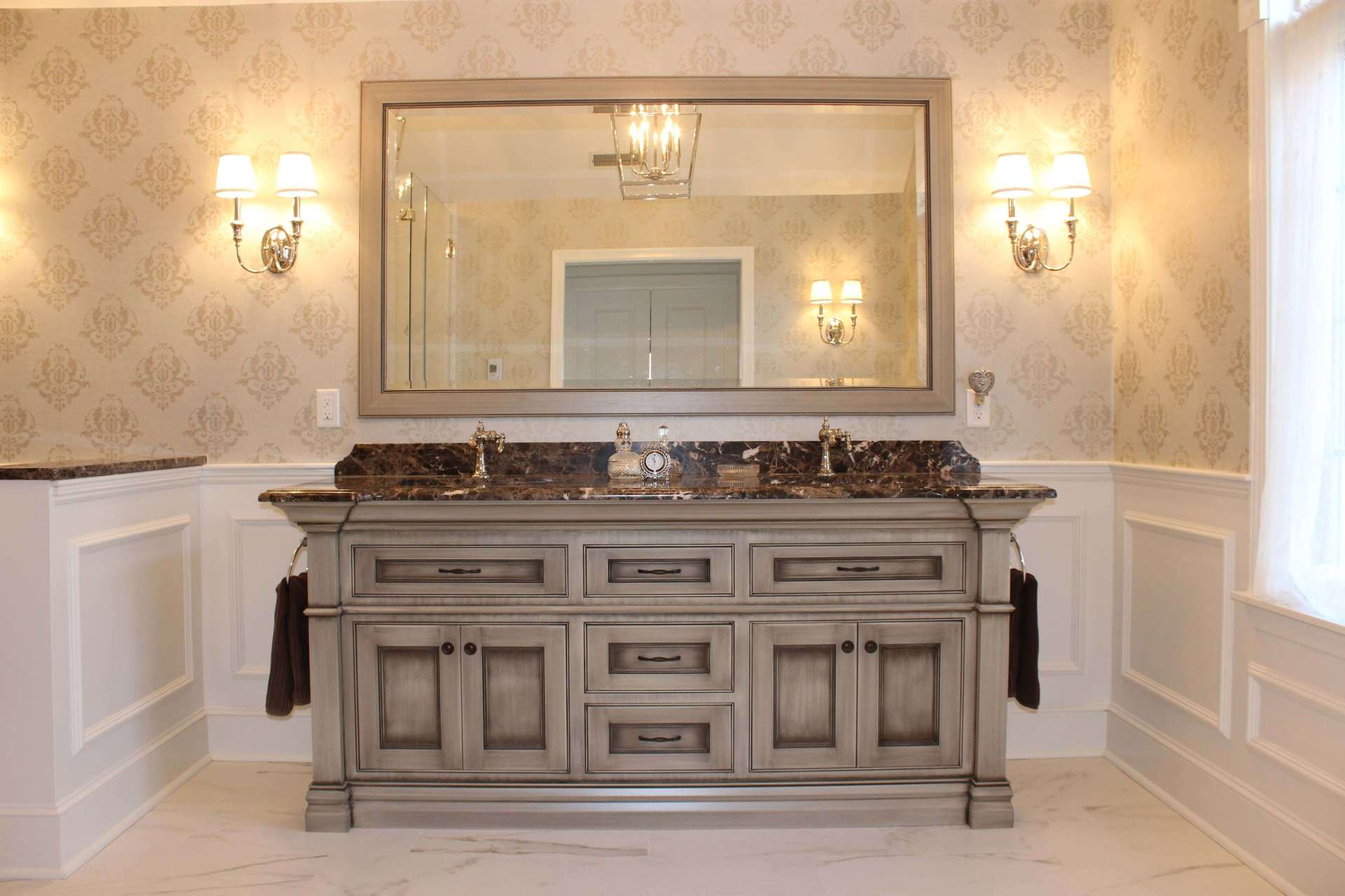 Elegant bathroom vanity with double sink, large mirror, and wall sconces in a beige tiled room