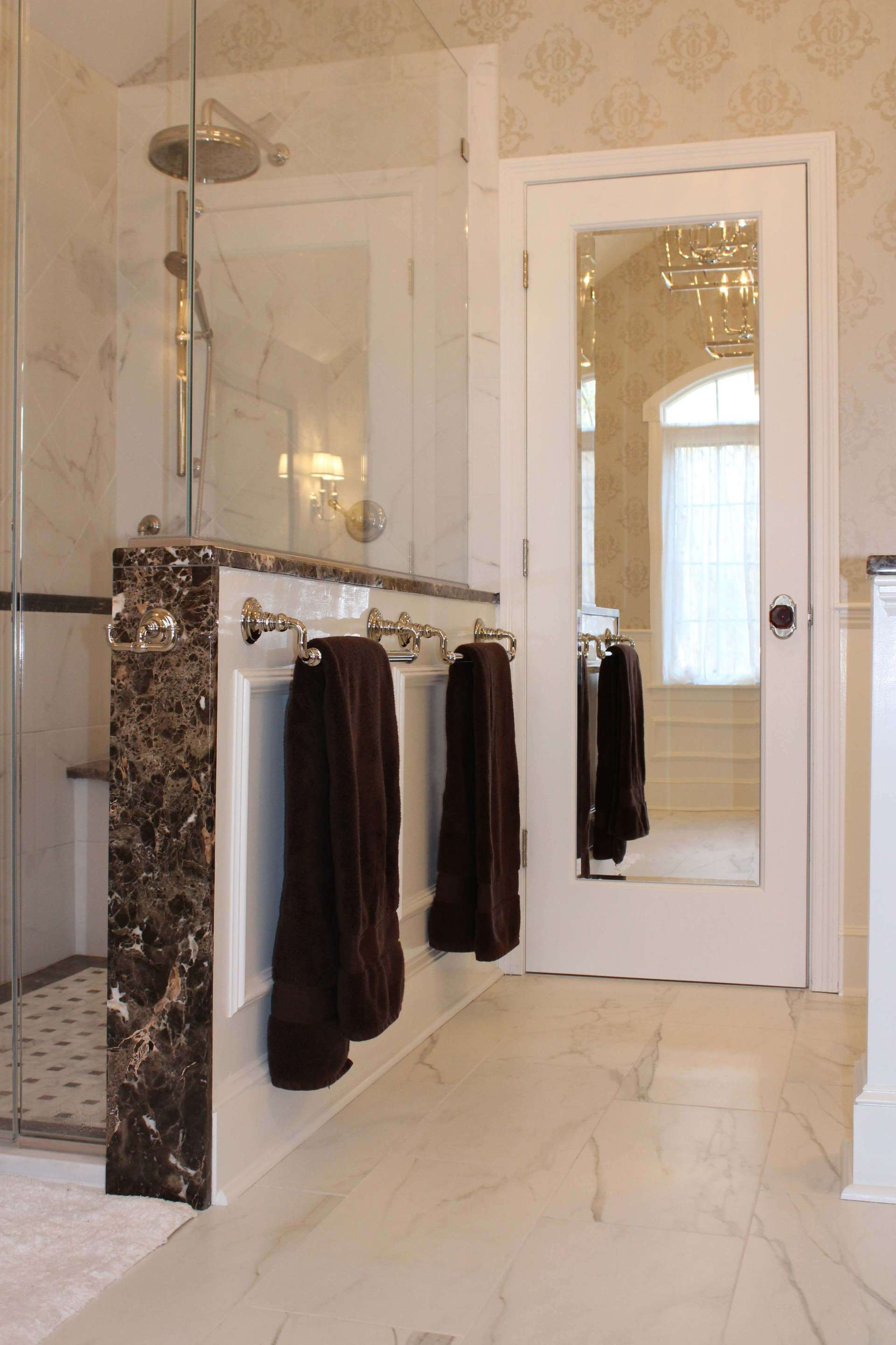 Elegant bathroom with marble shower, glass door, and dark towels hanging on a white towel bar