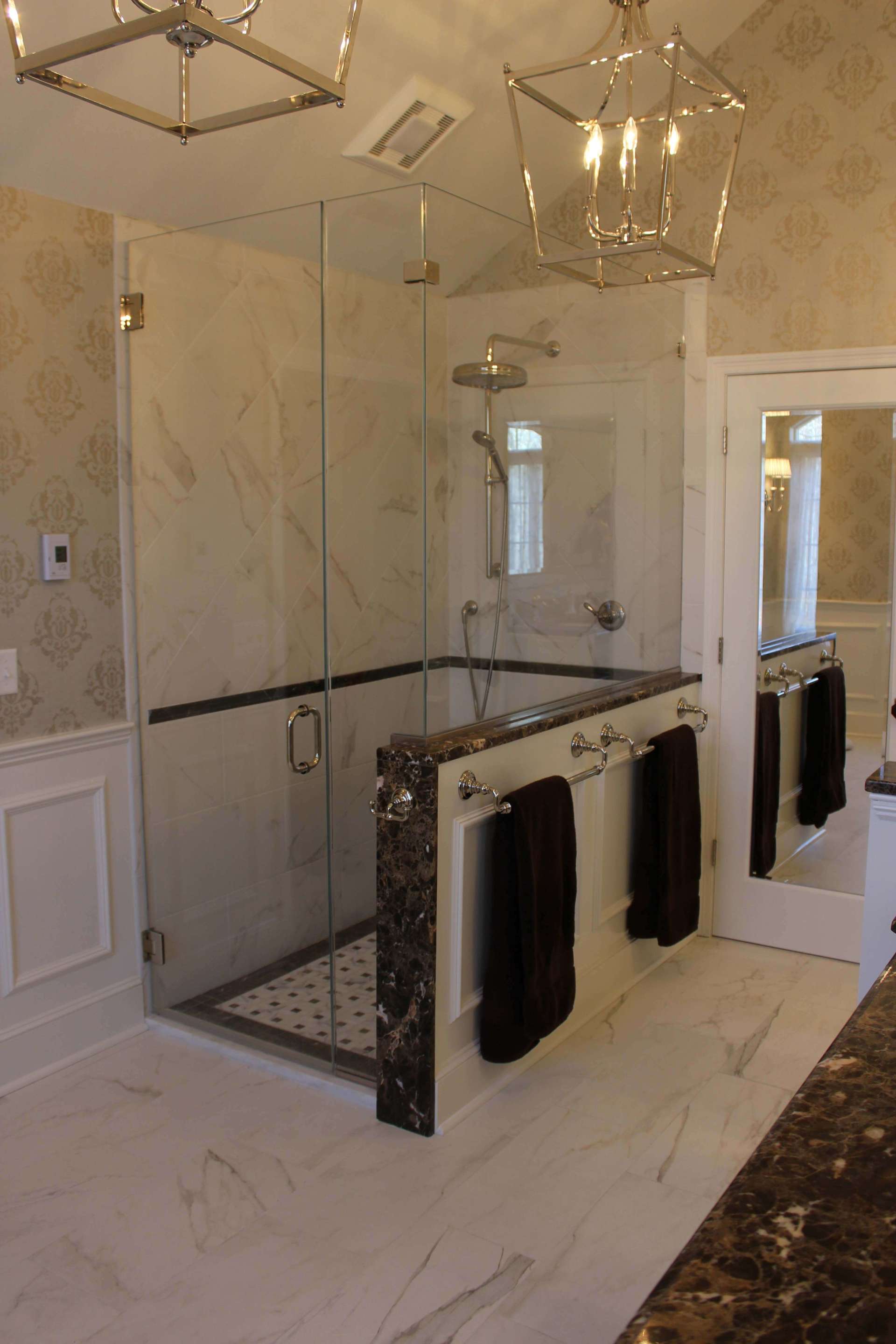 Luxury marble bathroom with glass shower, brass fixtures, and black towels hanging on a rail