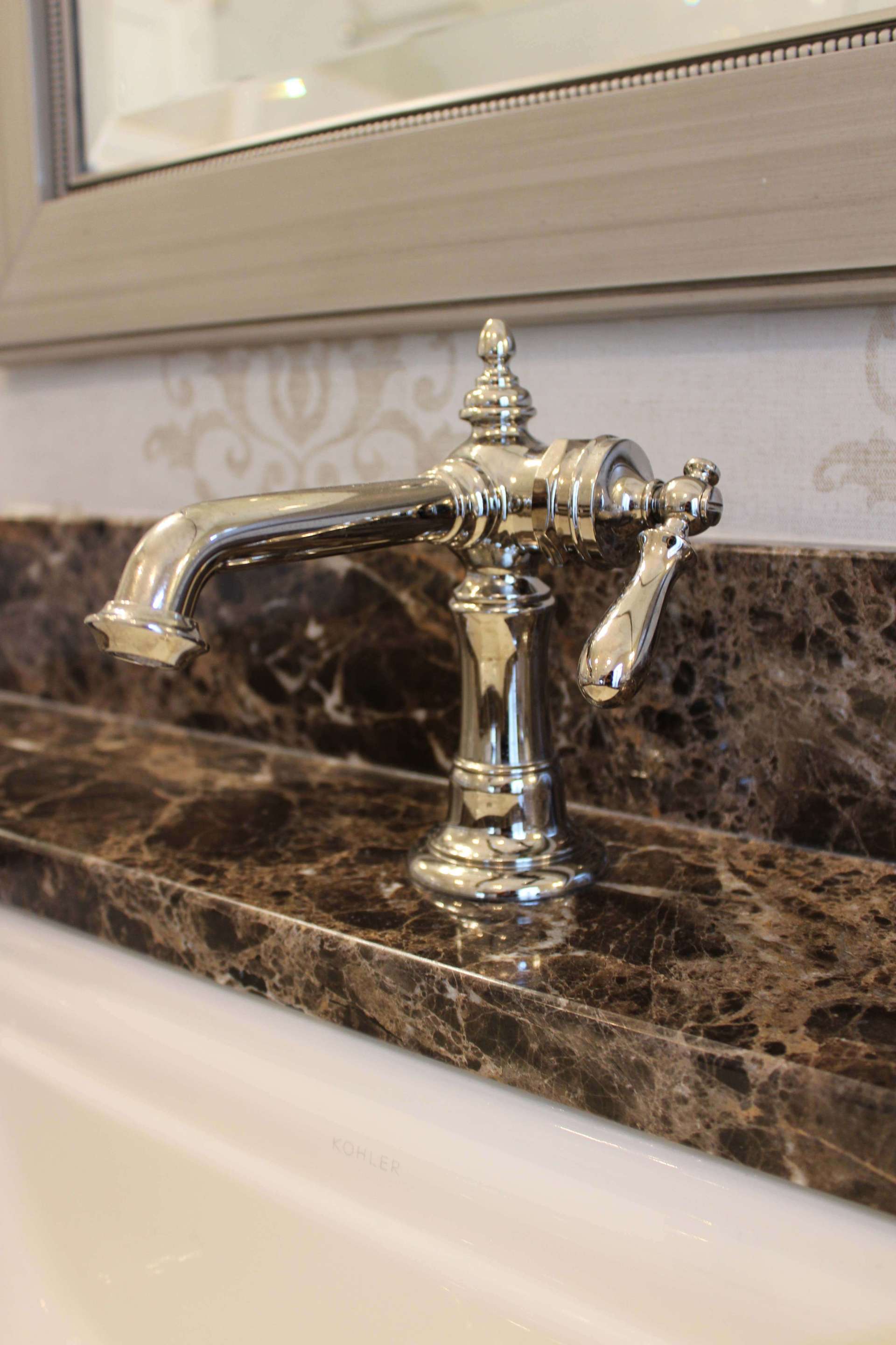Chrome faucet on a dark marble bathroom countertop under a mirror
