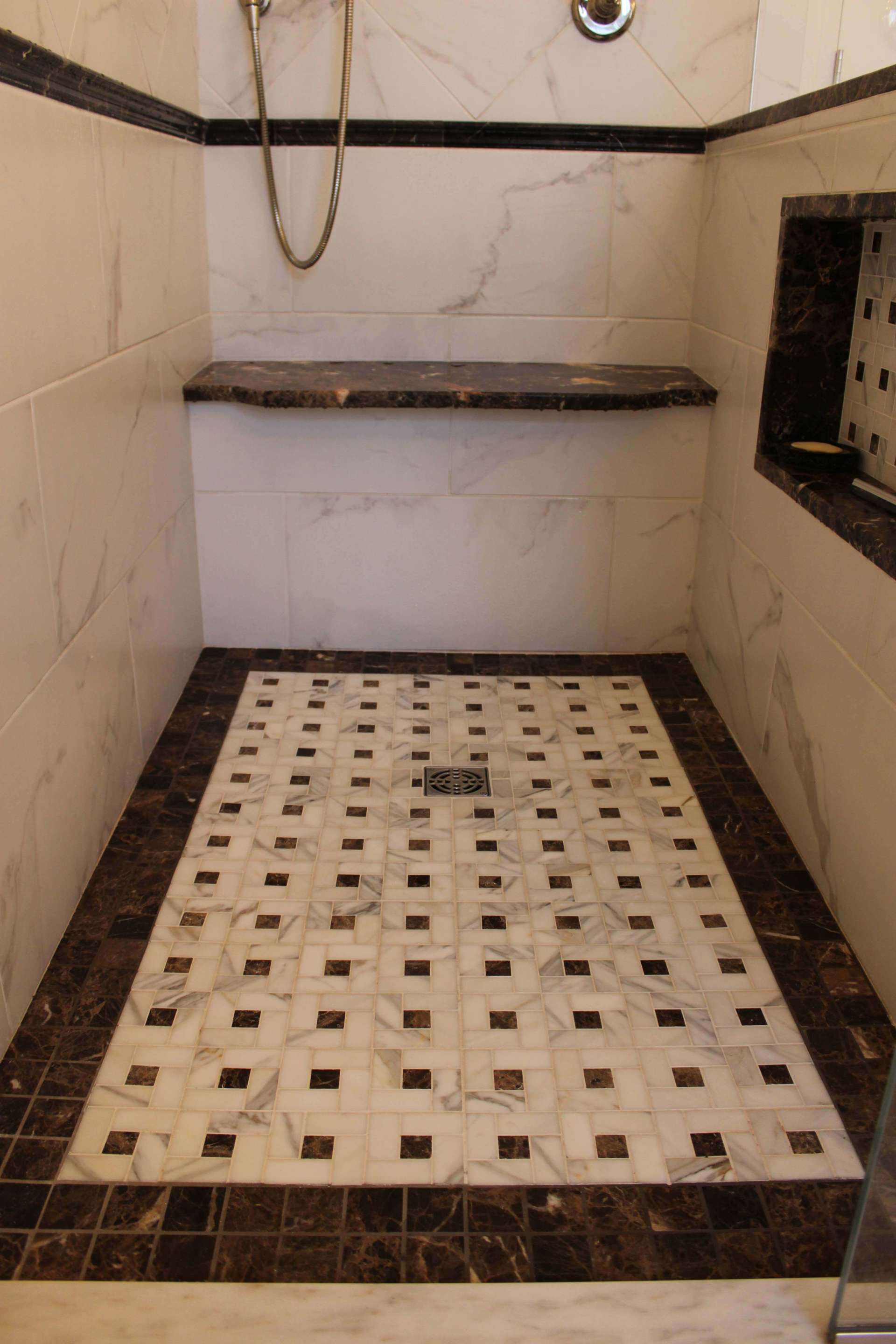 Small tiled shower stall with a built-in shelf and mosaic floor drain area.