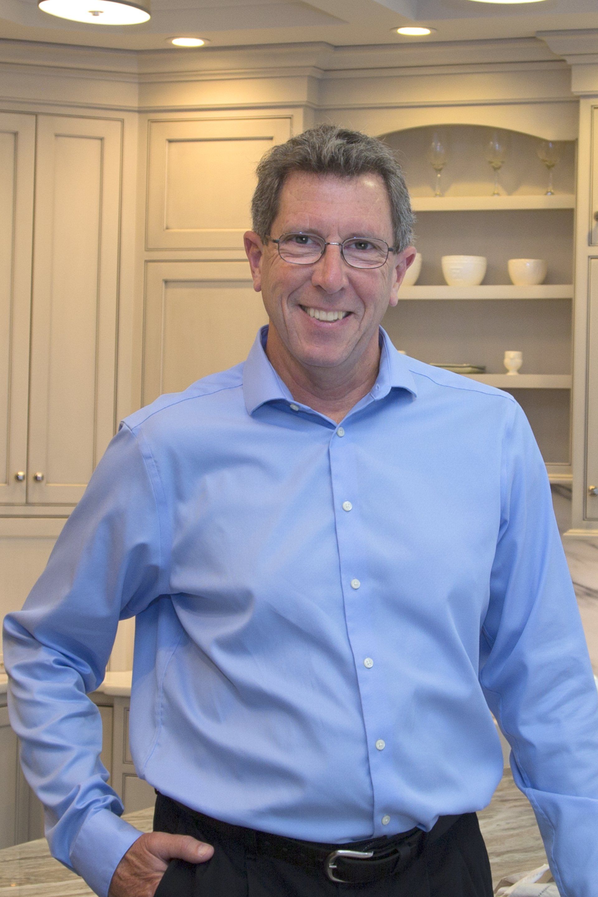 Man in a blue shirt smiling in a kitchen, standing in front of white cabinets.