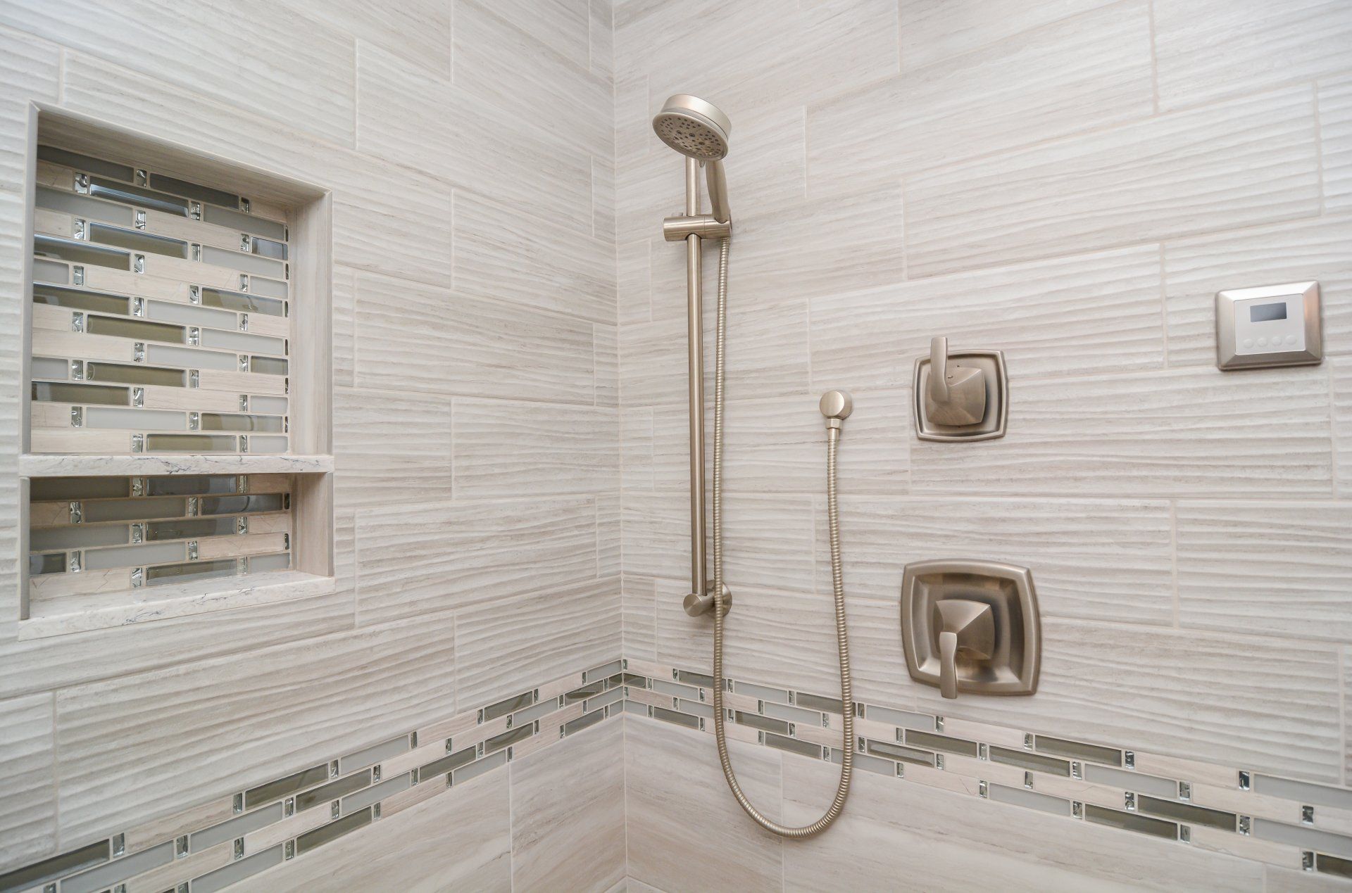 Modern tiled bathroom shower with handheld showerhead, grab bars, and built-in shelf niche