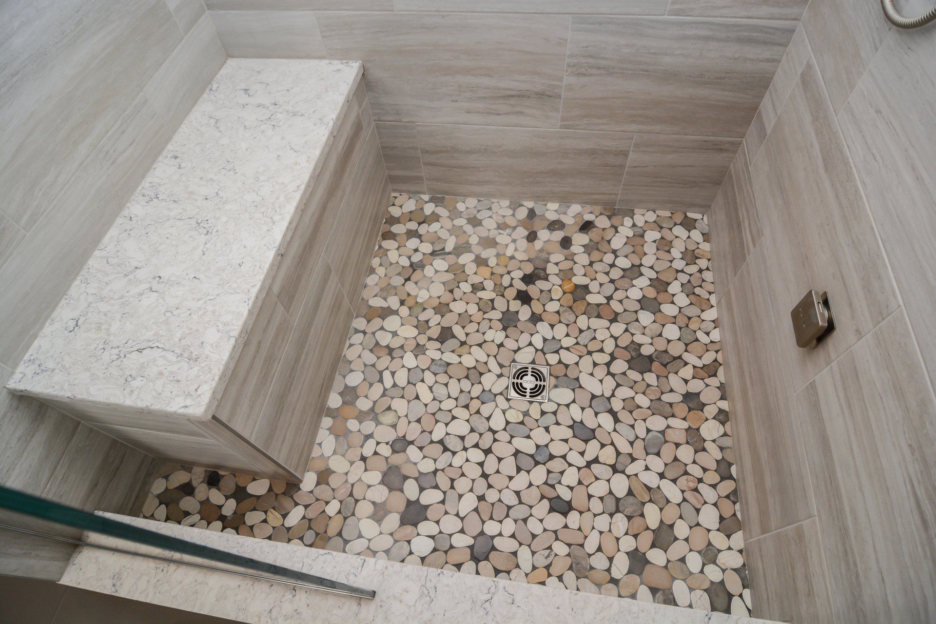 Small stone-tiled shower with a built-in bench and pebble floor, viewed from above.