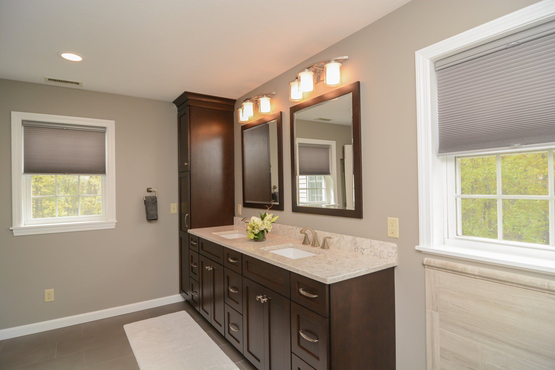 Spacious bathroom vanity with dark cabinets, large mirror, and two windows with blinds.