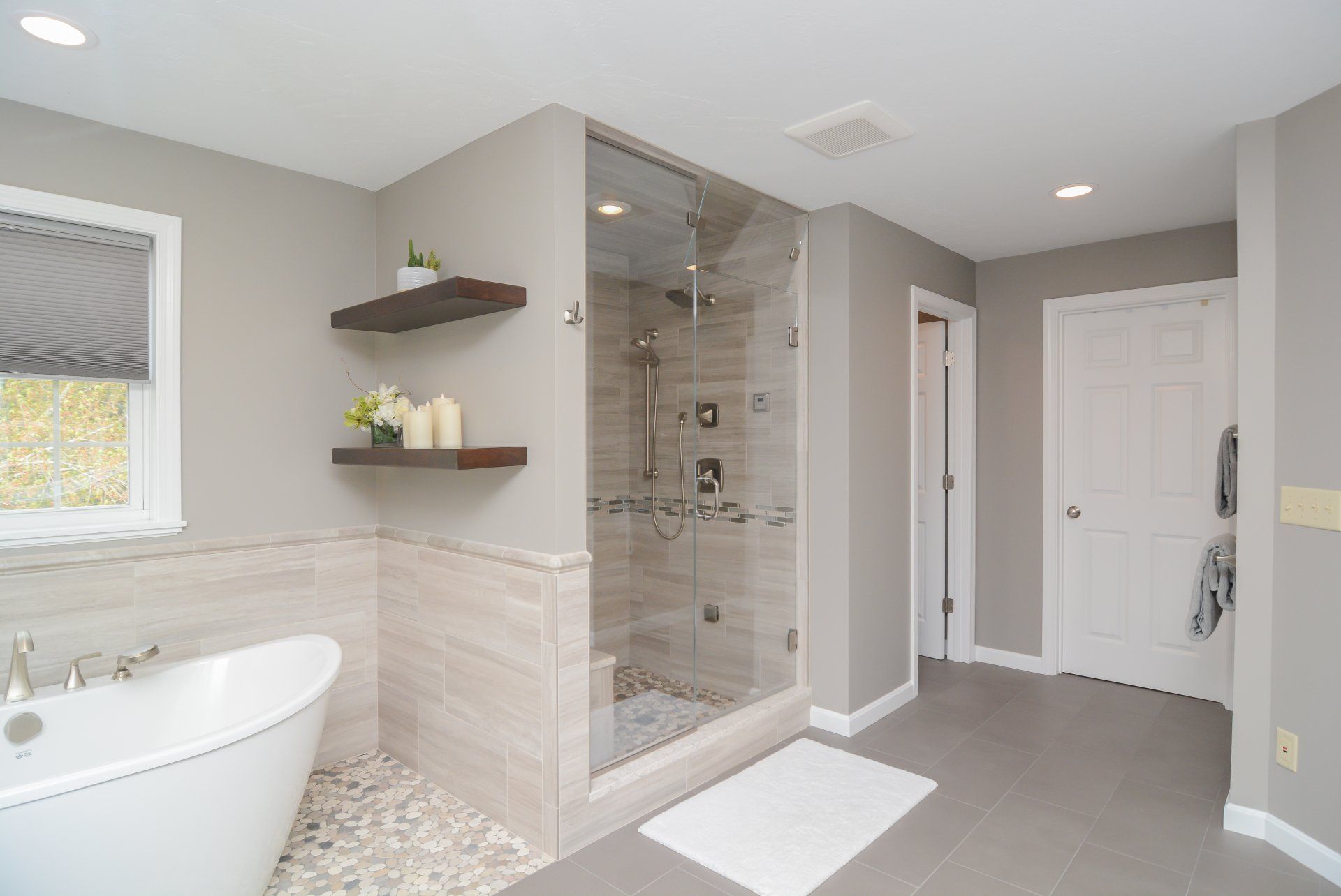 Bright modern bathroom with walk-in glass shower, freestanding tub, gray walls, and white tile flooring