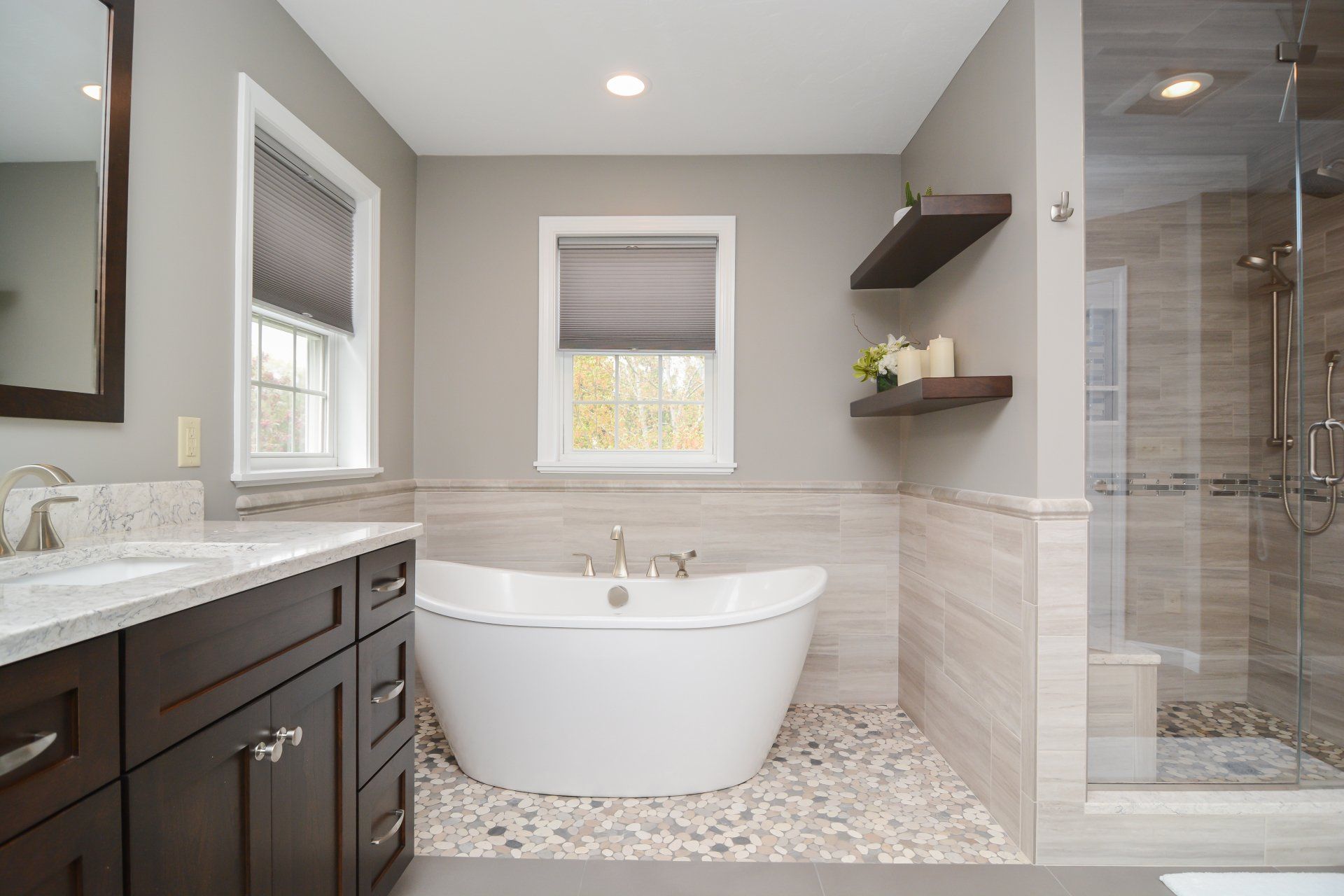 Modern bathroom with freestanding tub, dark vanity, gray walls, and glass shower stall